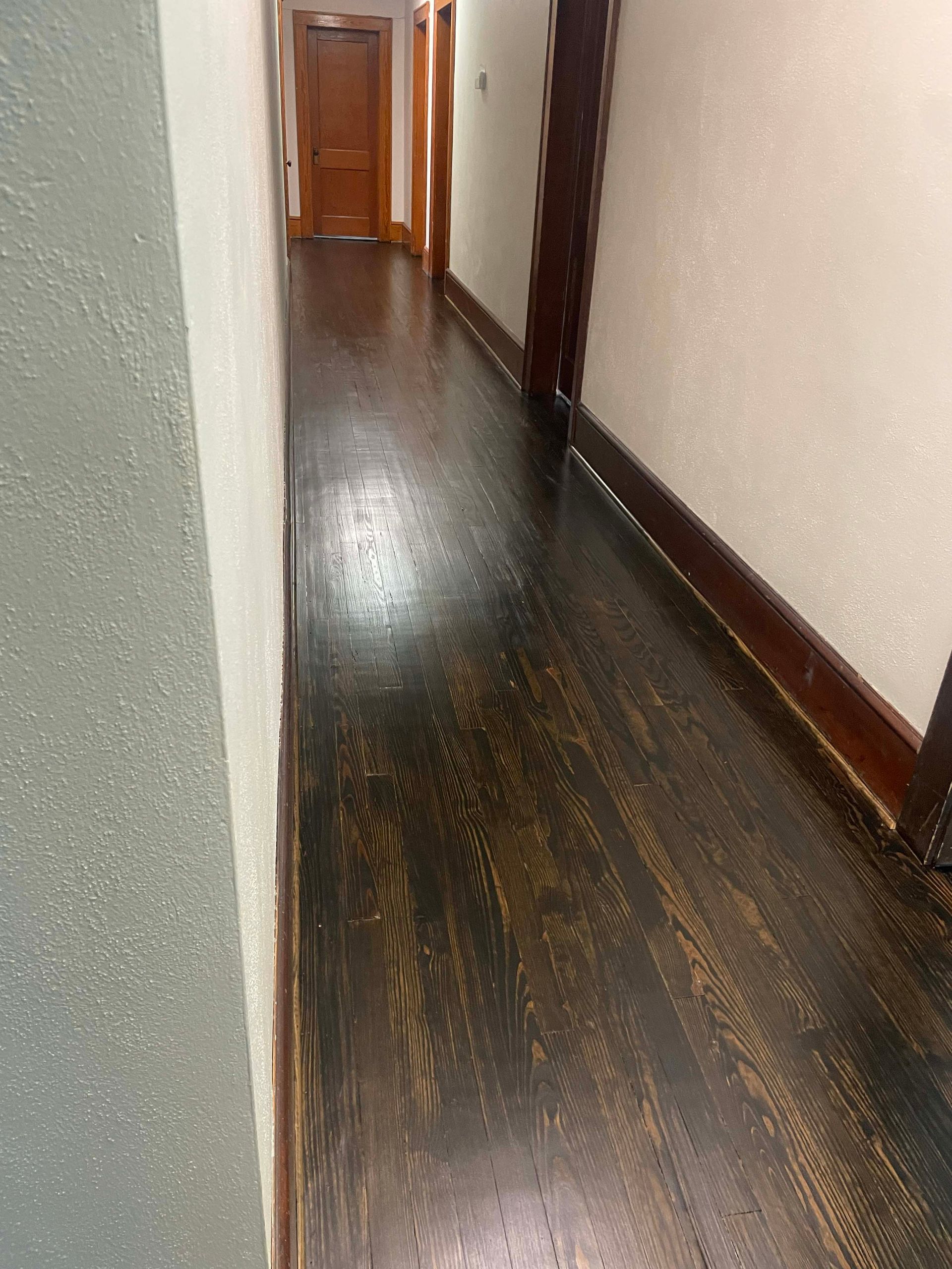 Dark wood floor in hallway with doors at the end. Beige walls with dark wood trim.