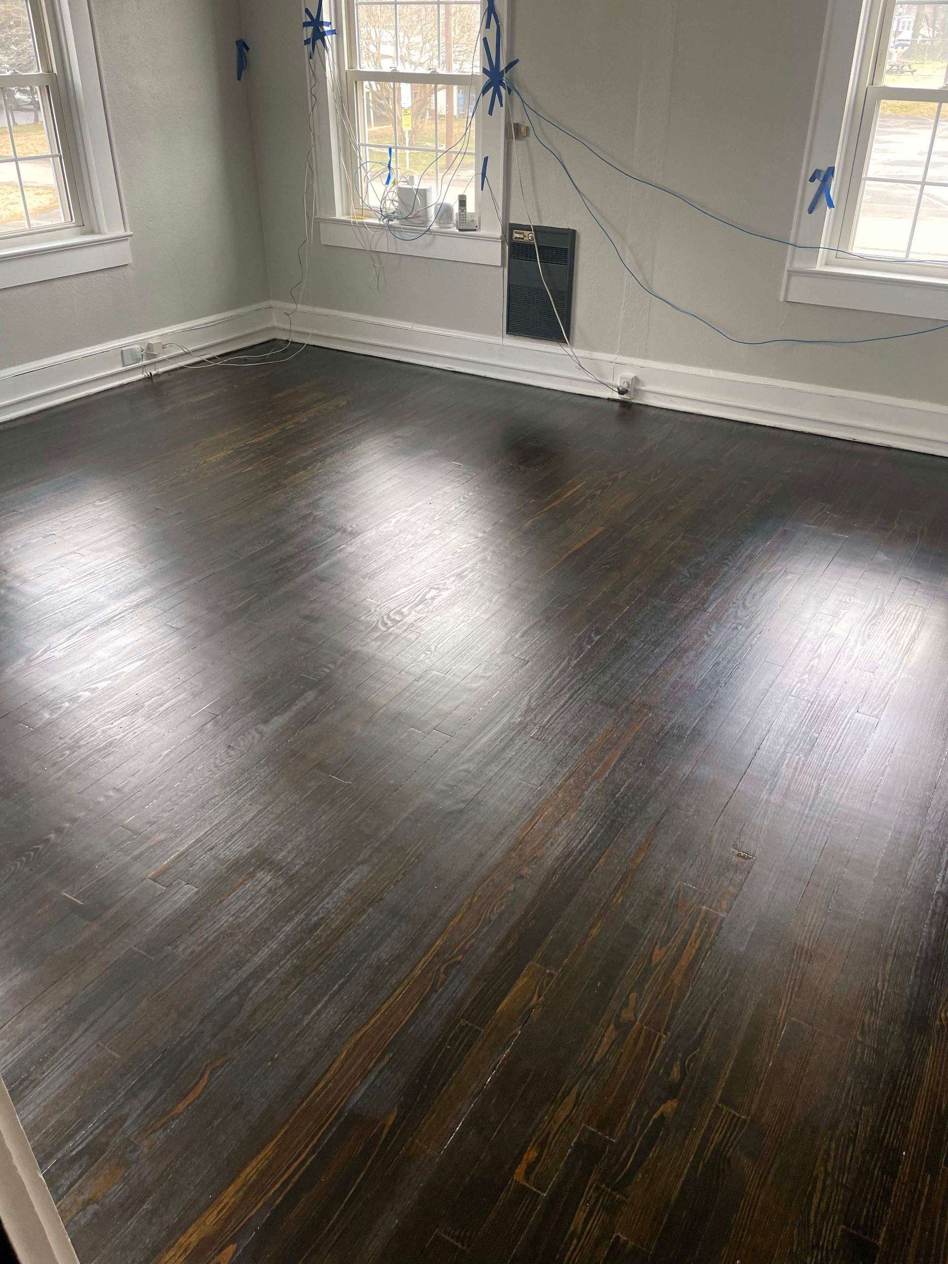 Dark stained hardwood floor in a room with white trim, windows, and gray walls.