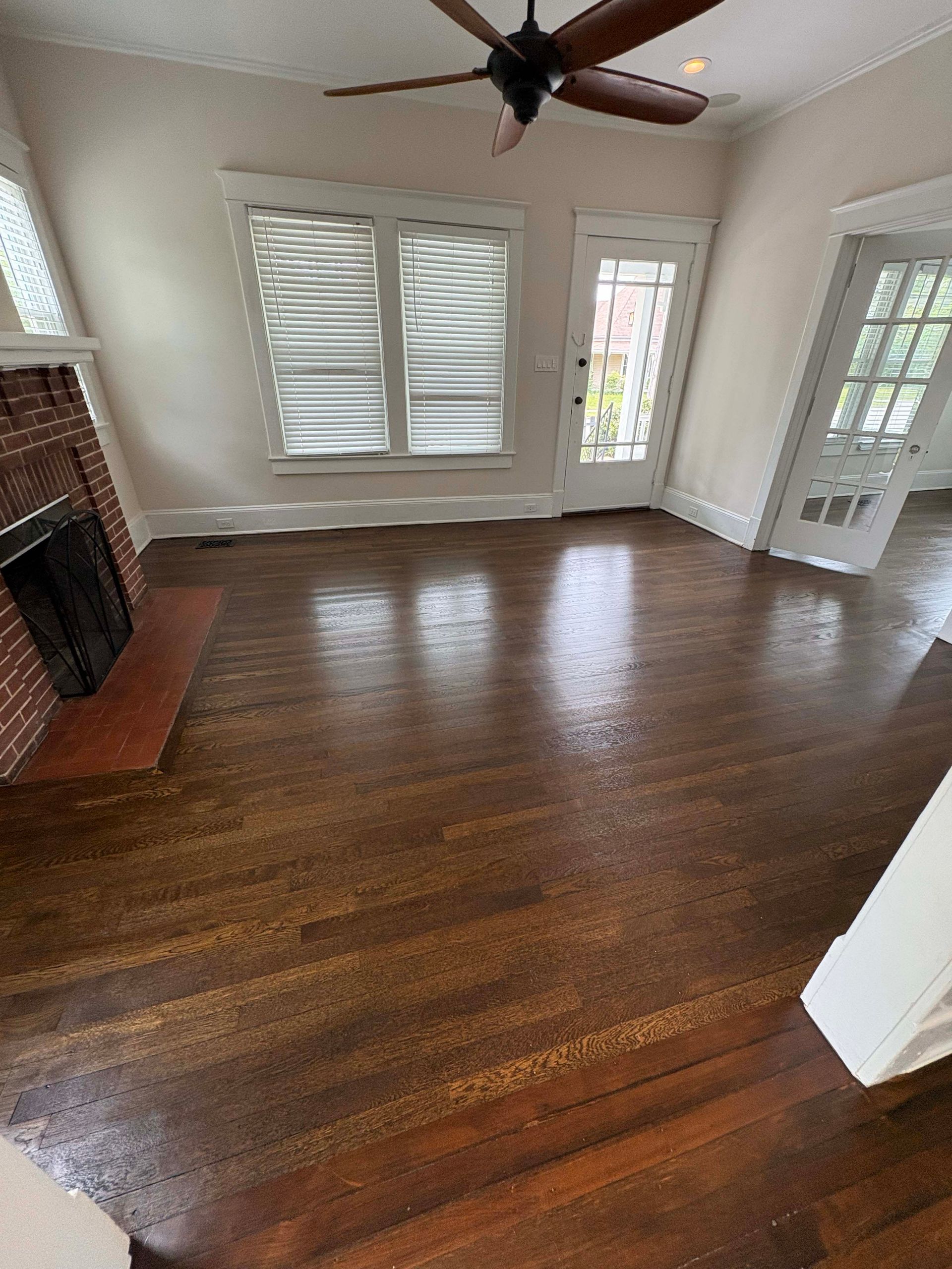 Living room with dark wood floor, fireplace, windows with shutters, and a door.