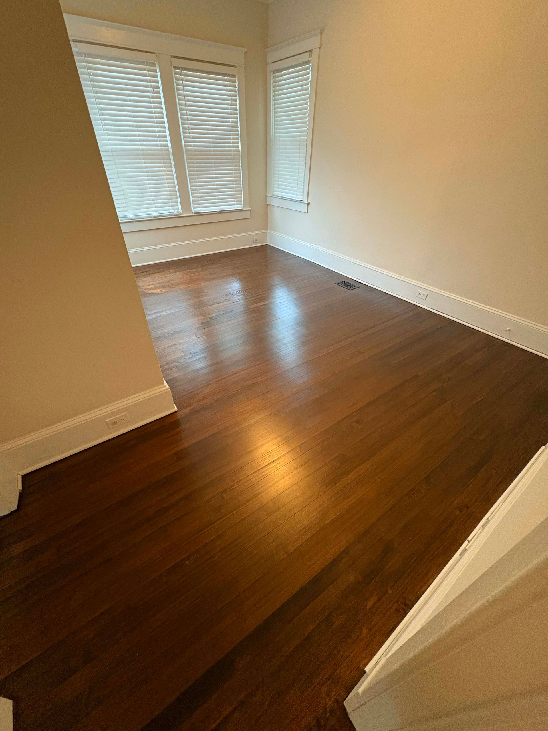 Empty room with dark wood floors, white trim, and a window with blinds.