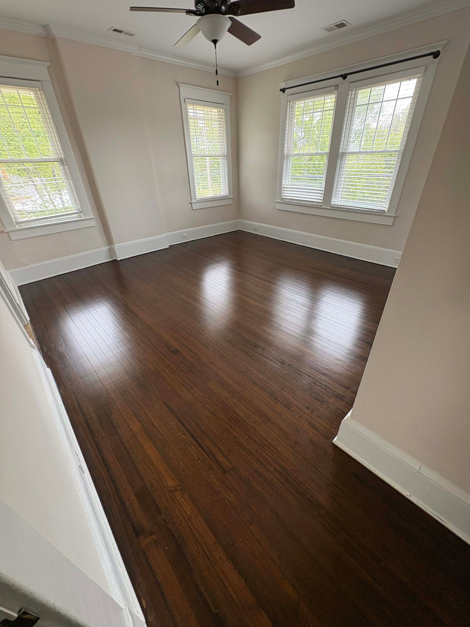 Empty room with dark hardwood floors, windows, and light-colored walls.
