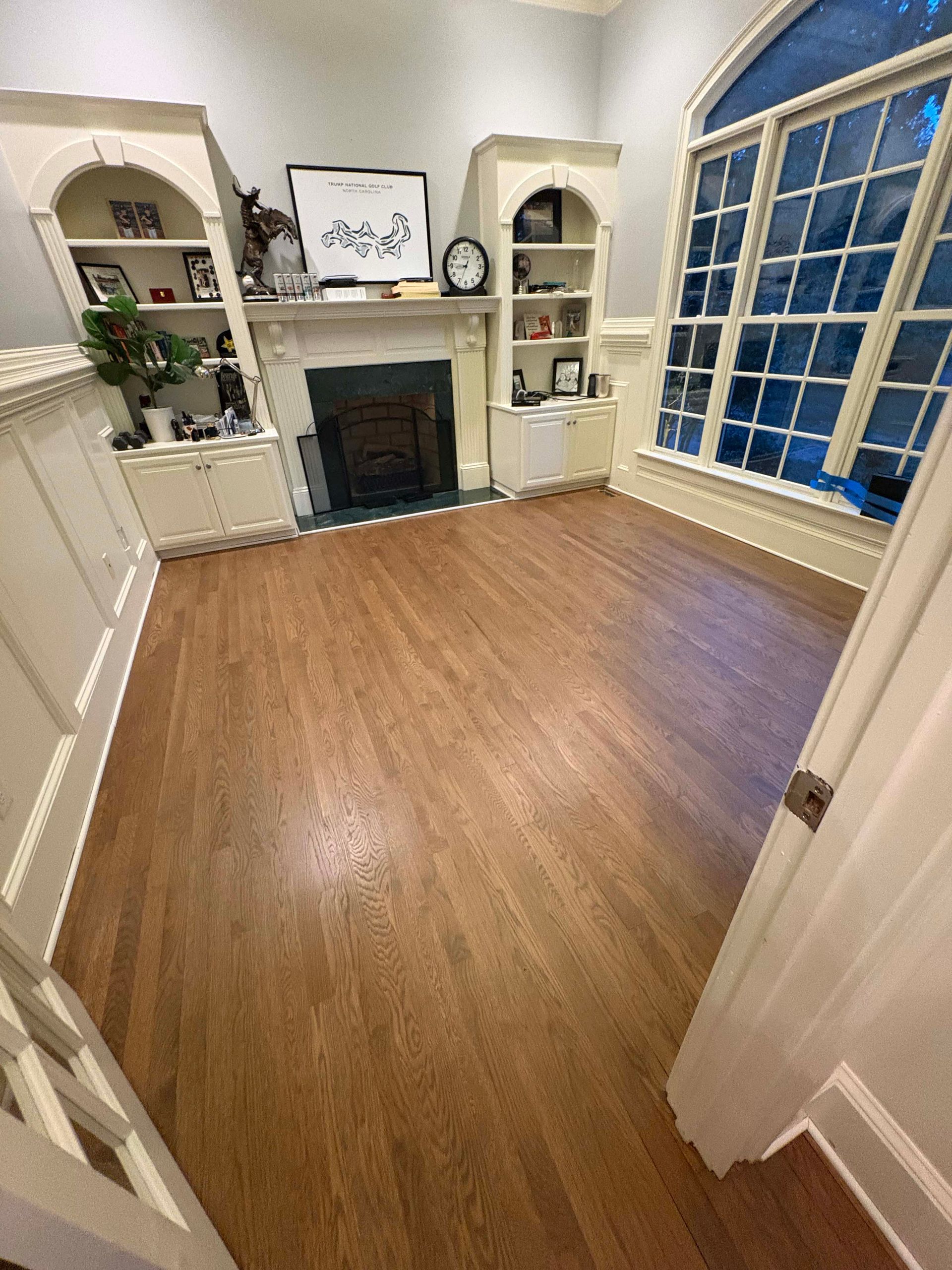 Empty room with hardwood floors, built-in shelving, fireplace, and arched window.