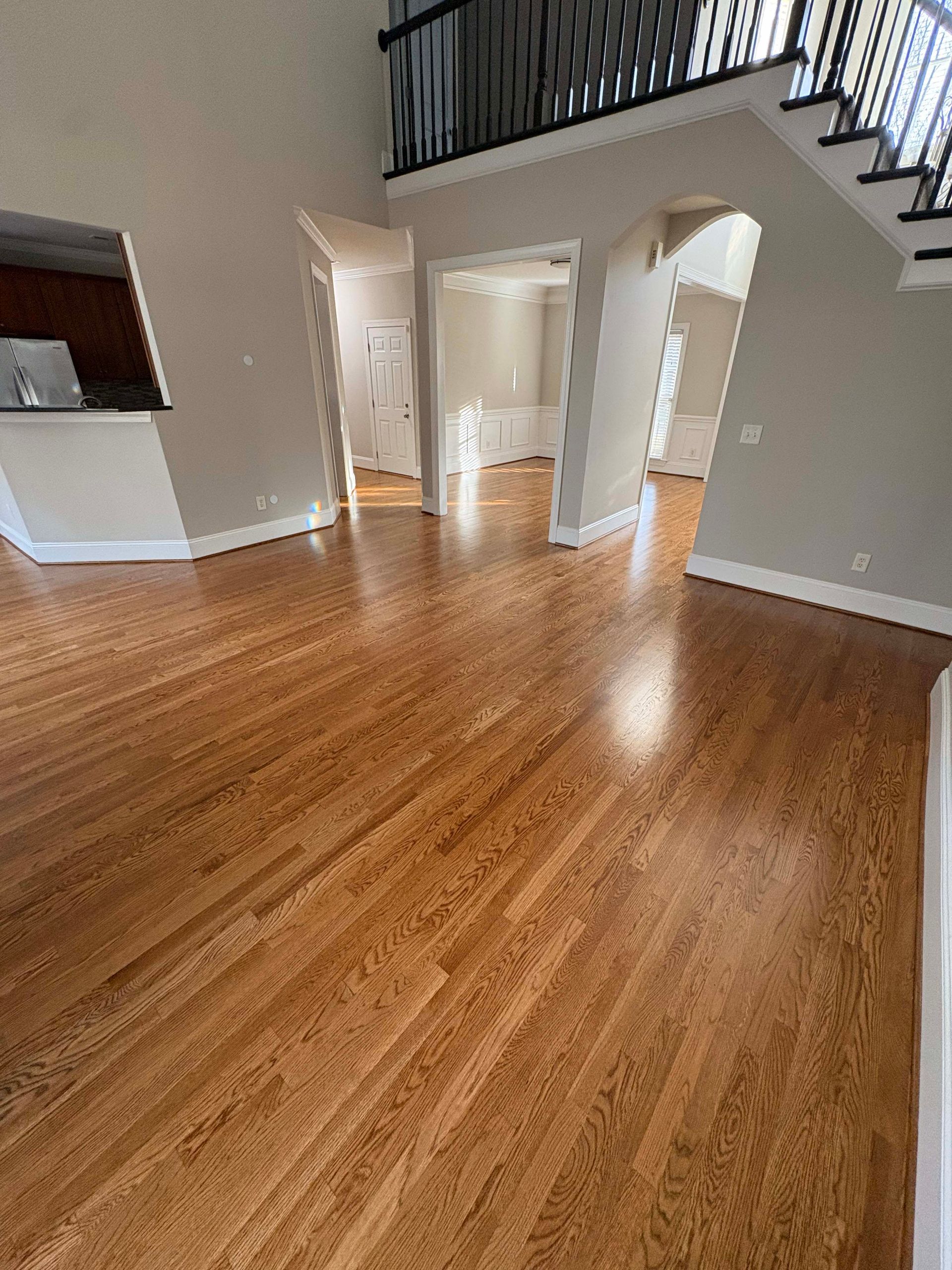 Hardwood floors in a house interior with tan walls, multiple doorways, and a staircase.
