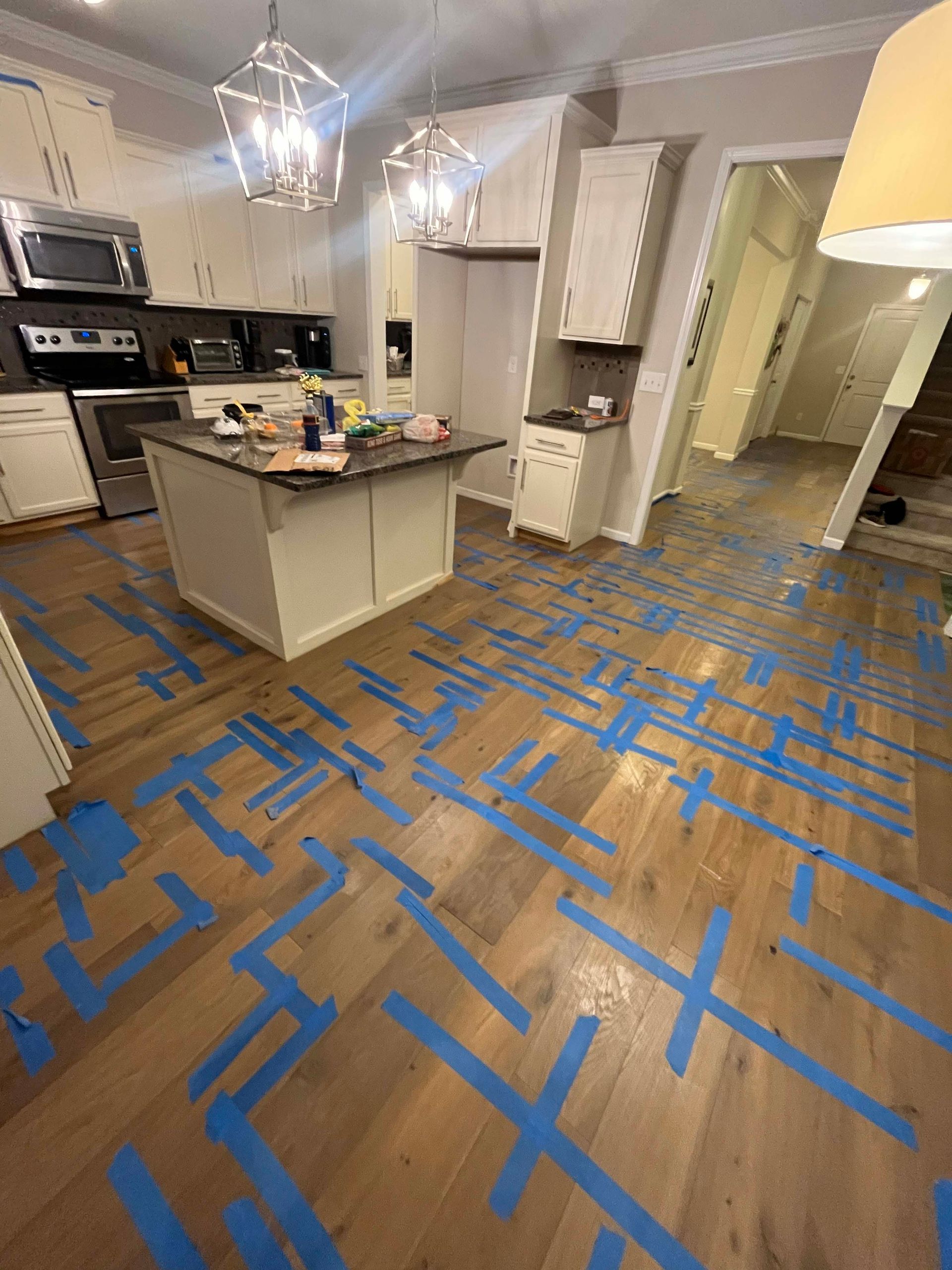 Kitchen with hardwood floors covered in blue tape, cabinets, and island.