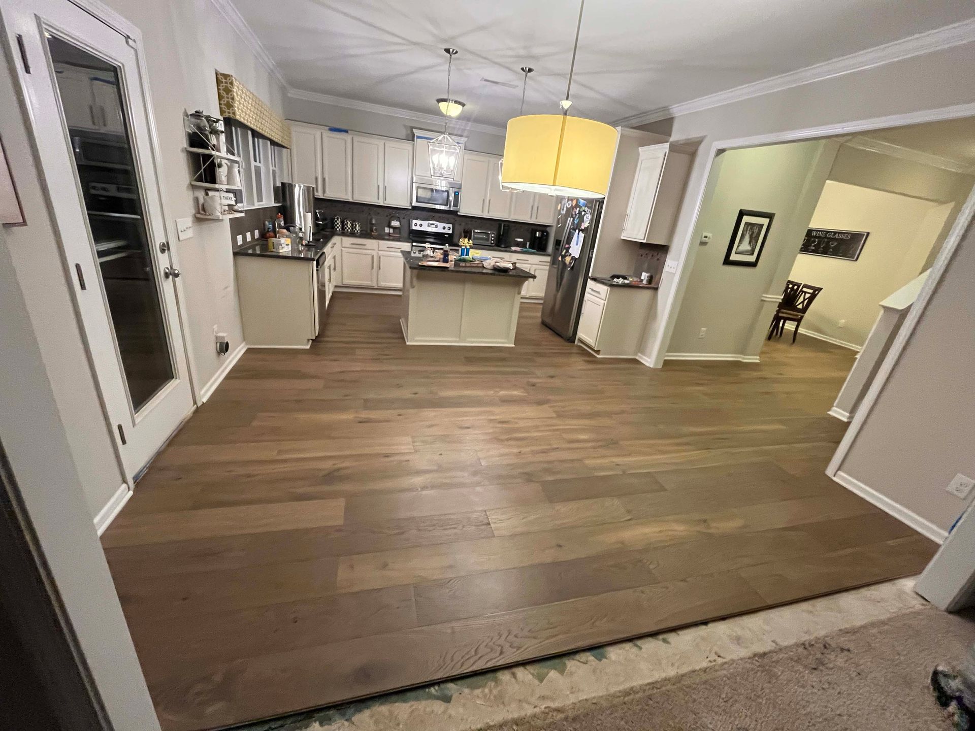 Hardwood floors installed in a kitchen and dining area. Beige cabinets, island, and appliances.
