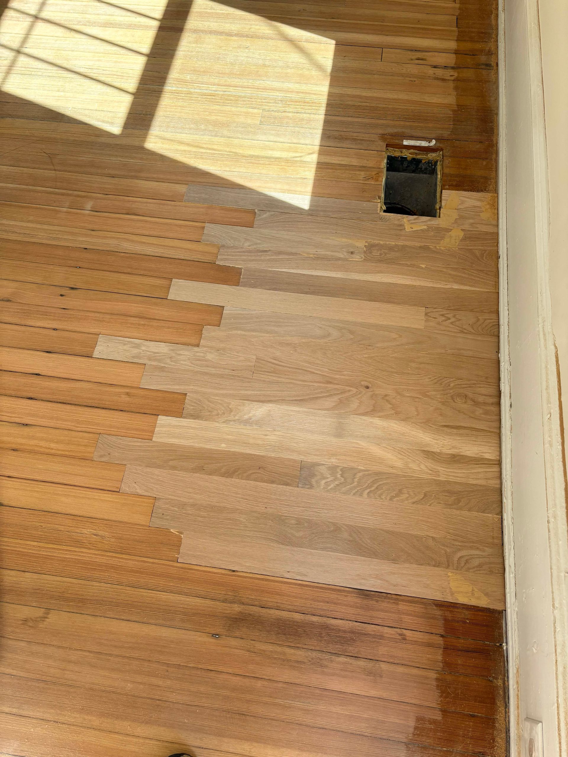 Hardwood floor with sunlit patches and a missing vent cover.
