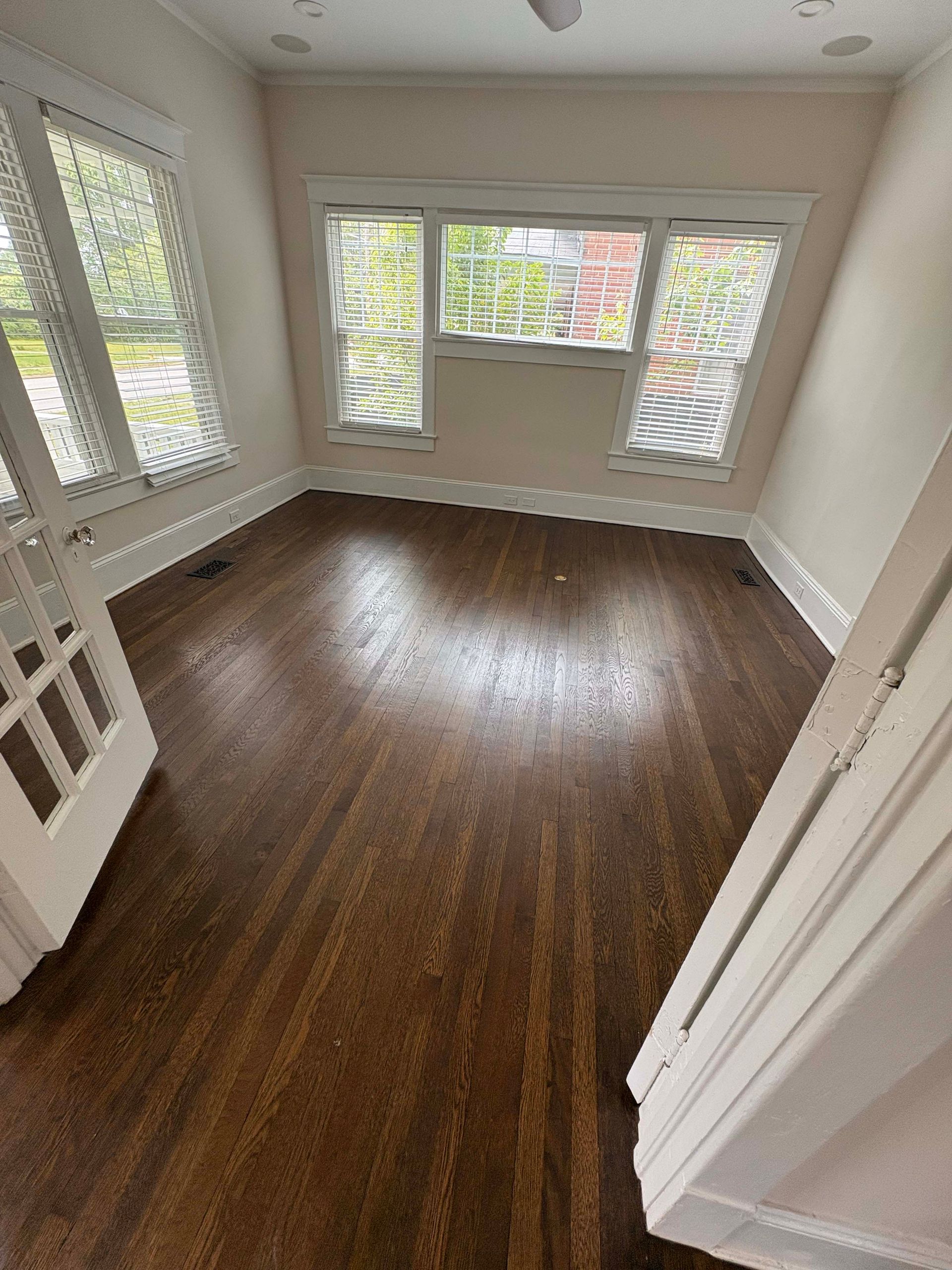 Empty room with hardwood floors, white trim, and windows; natural light.