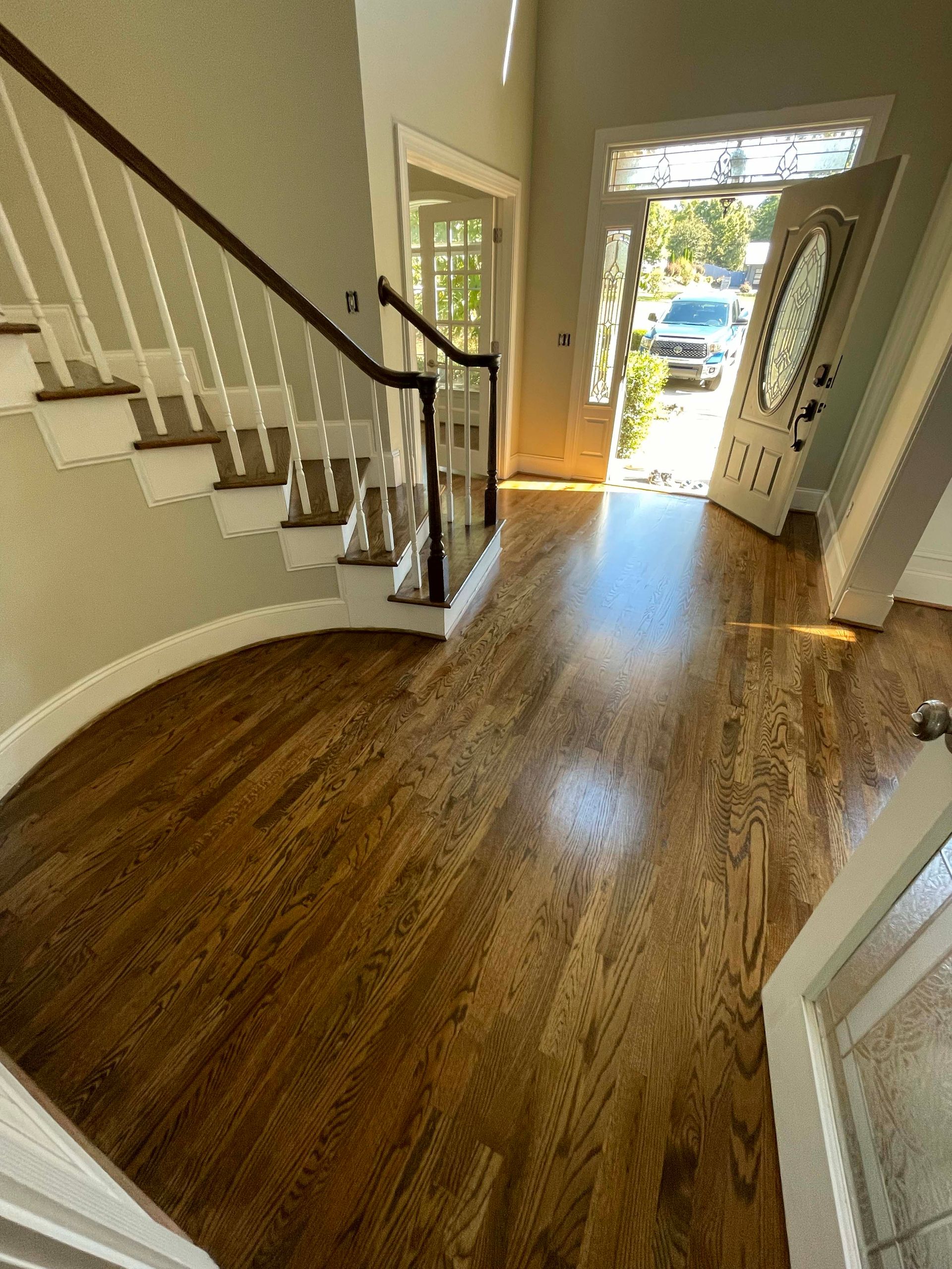 Wooden floor entryway with stairs and open front door.