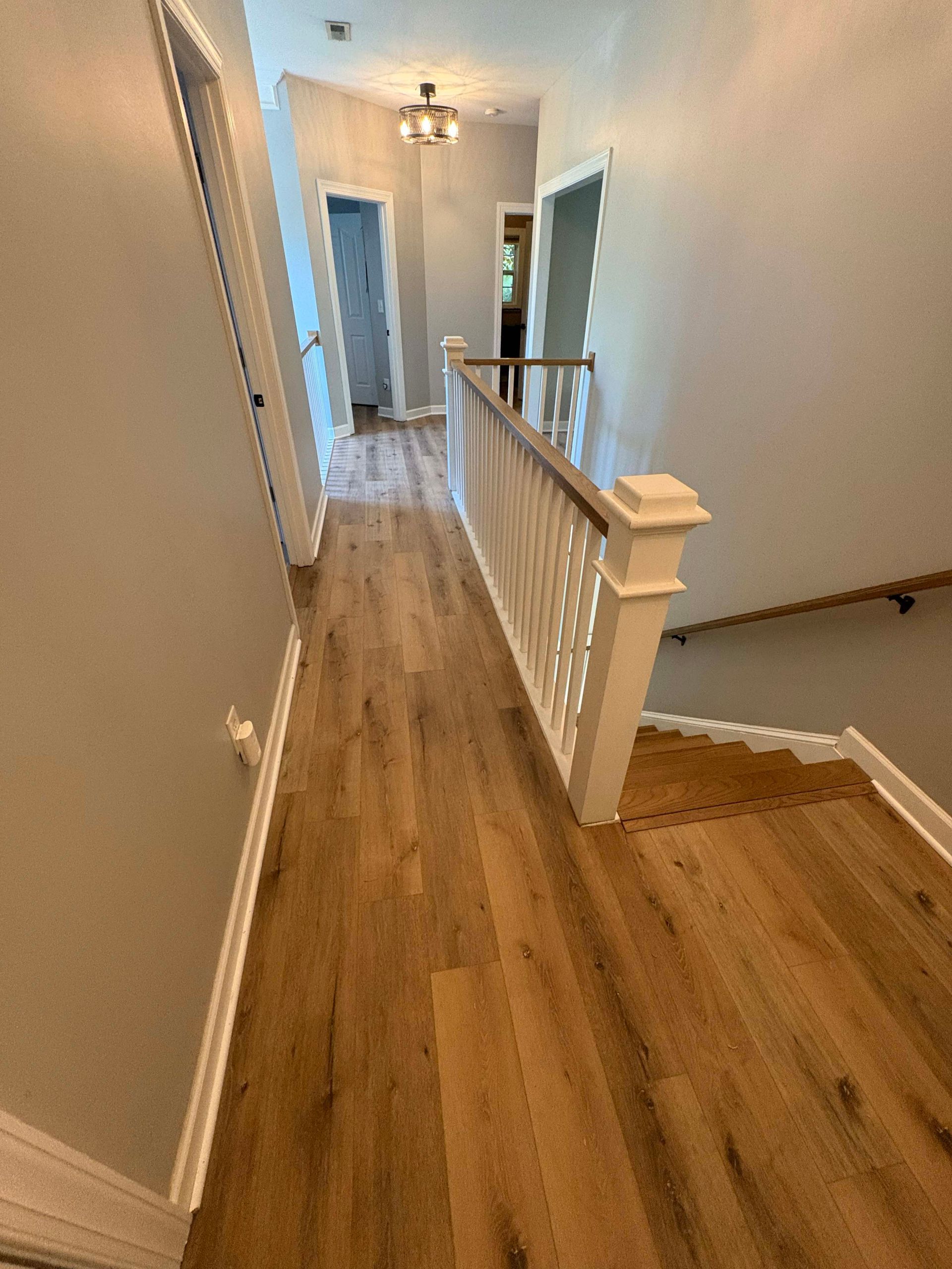 Hallway with wood floors, railing, stairs, and doors, painted walls, and overhead lighting.