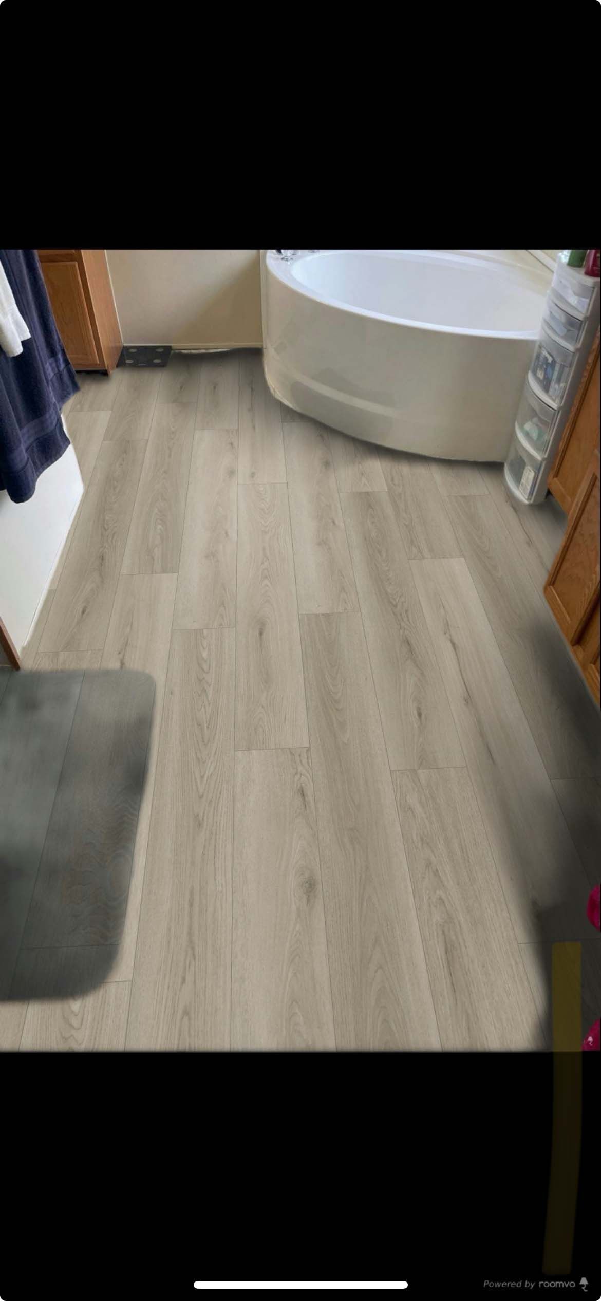 Bathroom with light wood-look flooring. White bathtub and brown cabinets.