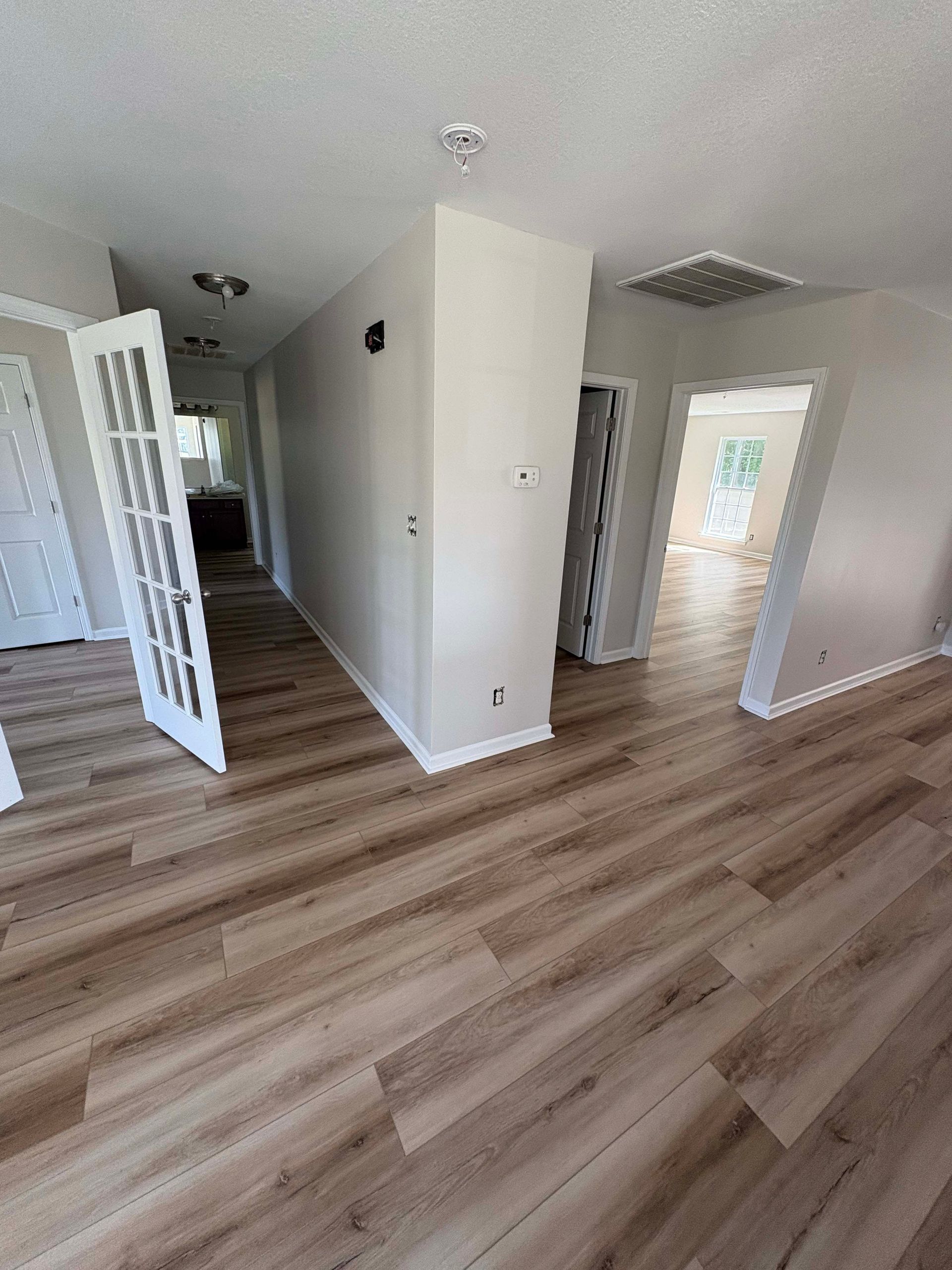 Interior view of a hallway with wood-look flooring, white walls, and open doorways.