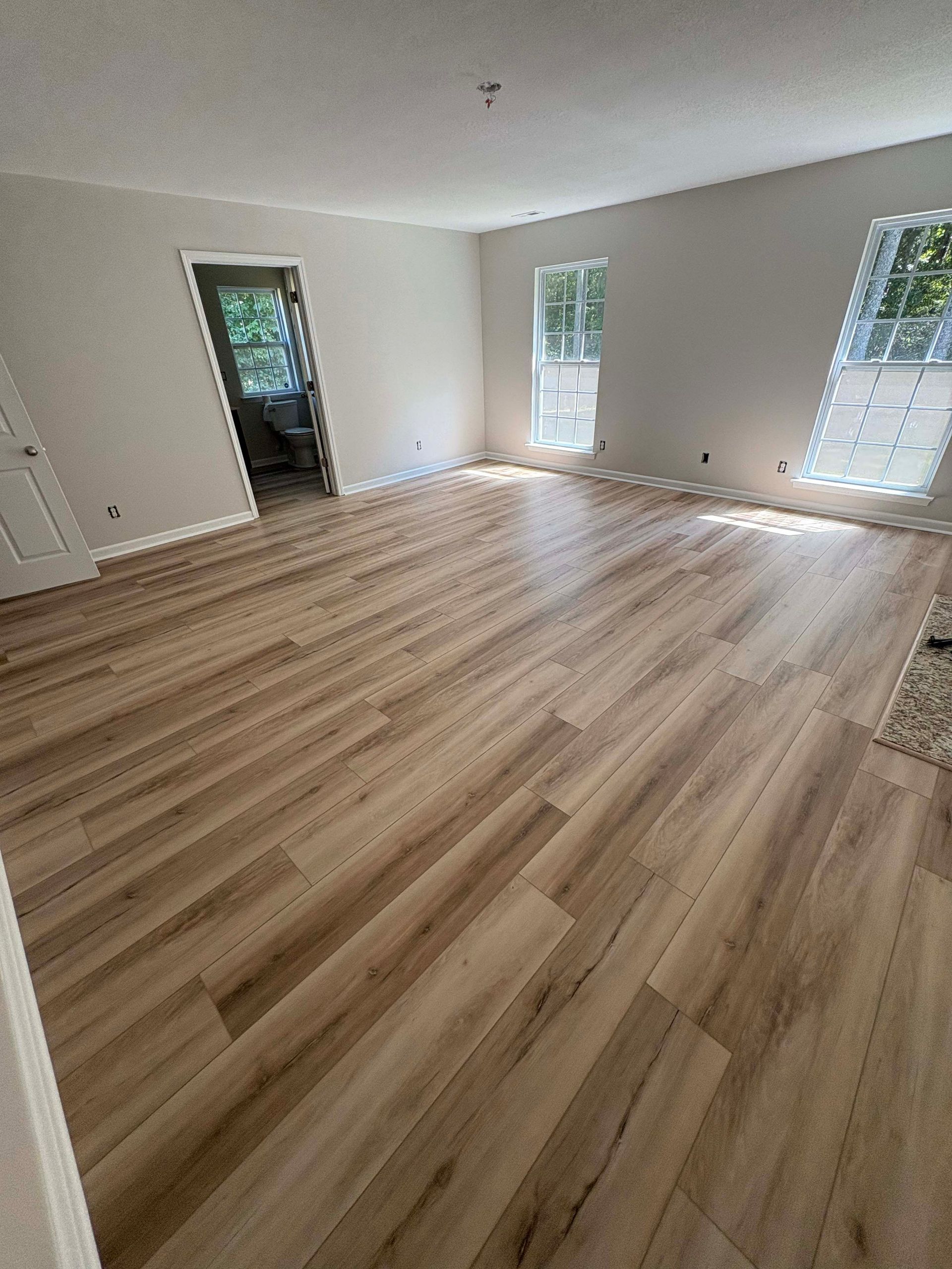 Empty room with light wood-look flooring, white walls, and two windows.