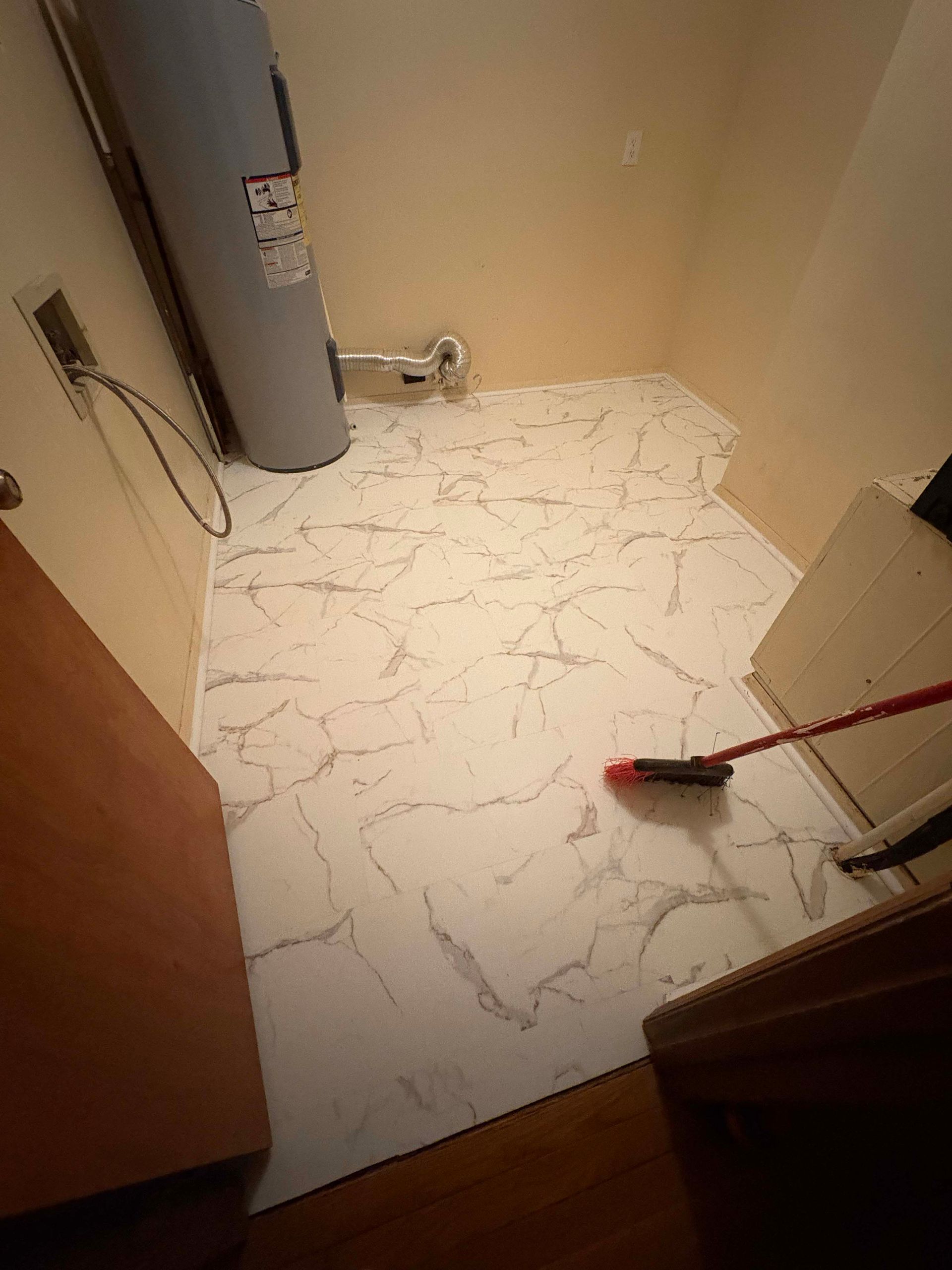 Laundry room with new white marble-look flooring. A water heater and a broom are visible.