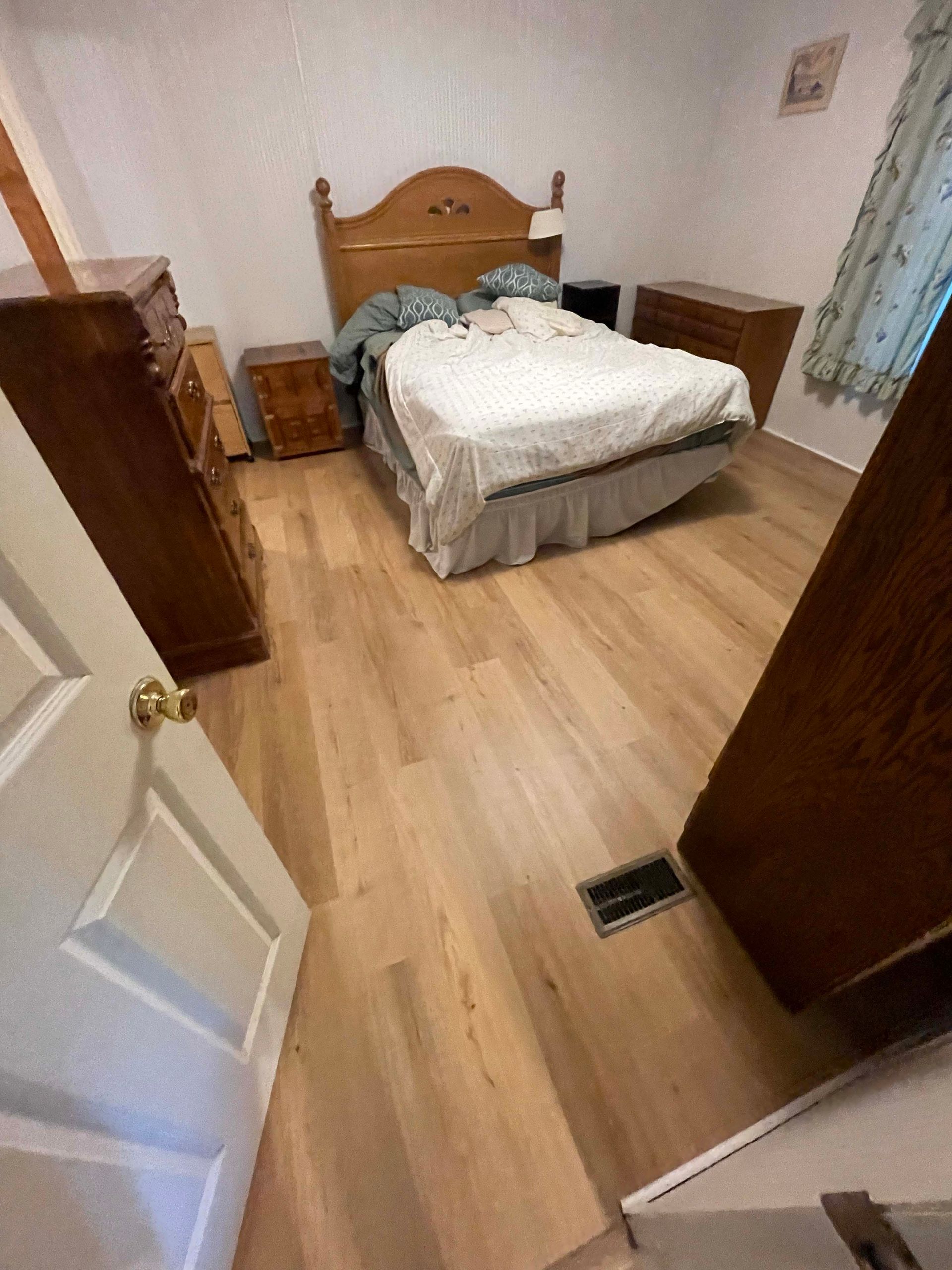 Bedroom with wood flooring, bed, dressers, and a partially open door.