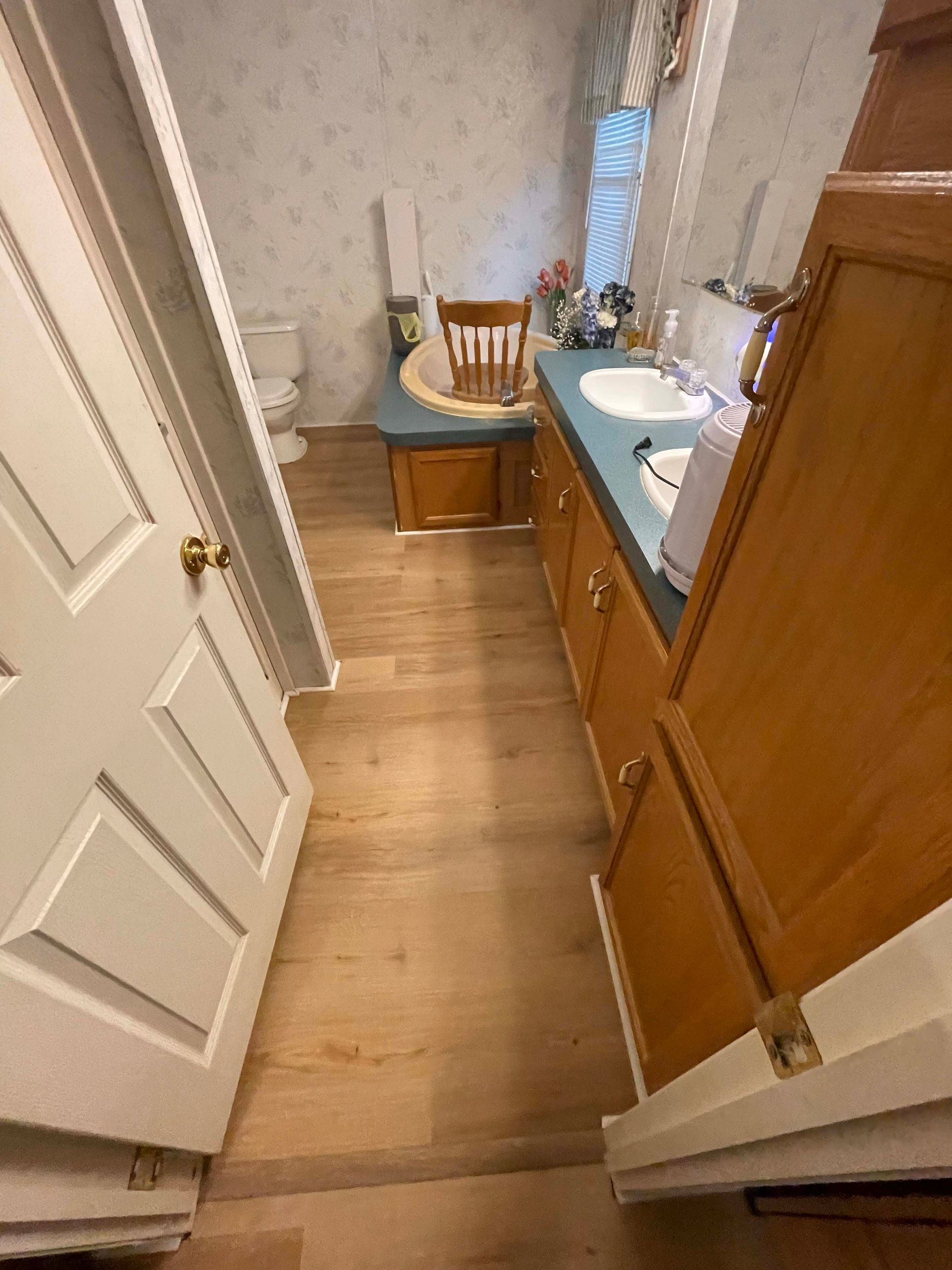 Bathroom interior with hardwood floors, a vanity, toilet, and chair. Light colors dominate the space.