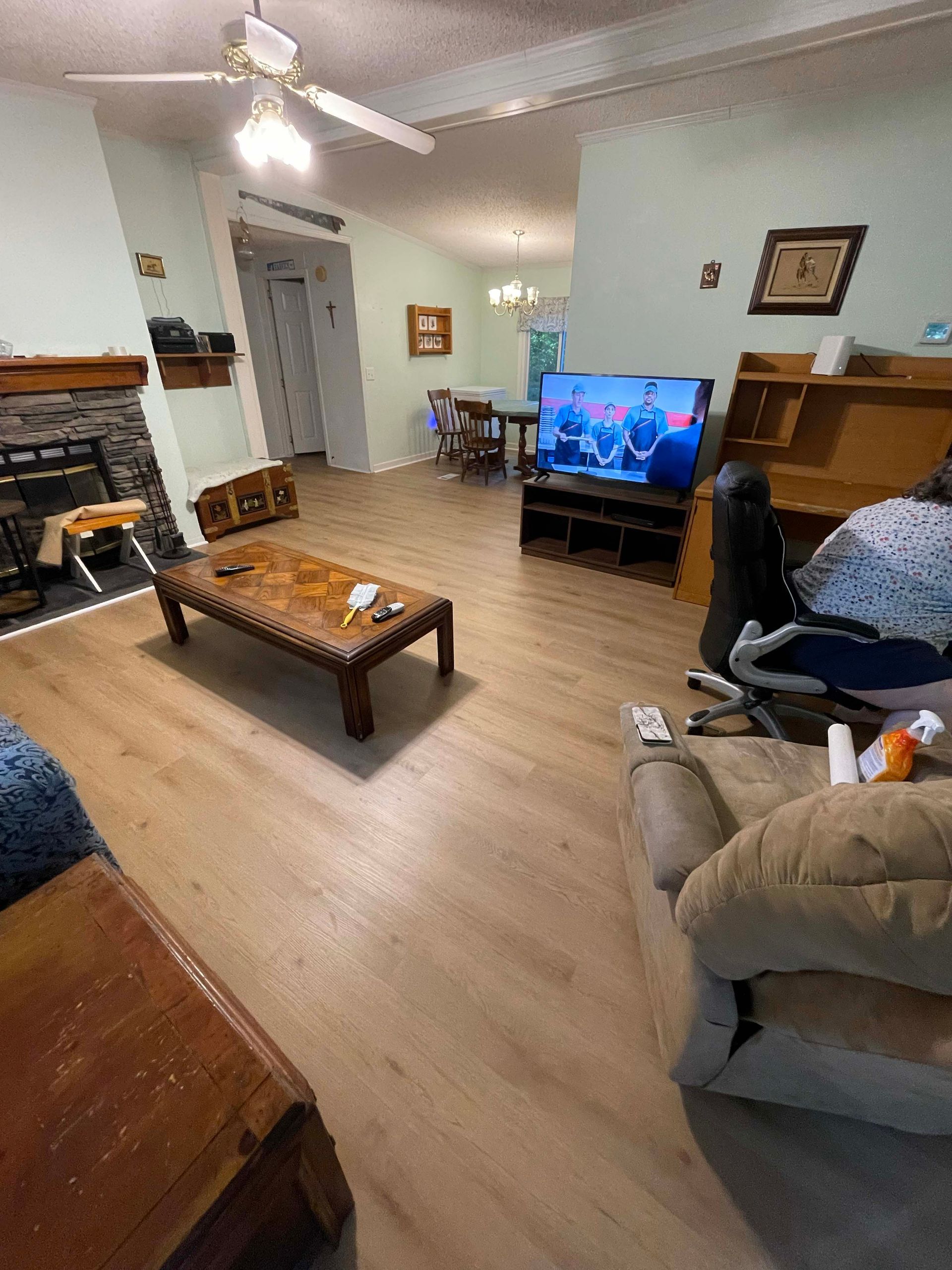 Living room with light wood floors, fireplace, and TV. Furniture includes a coffee table, sofa, and recliner.