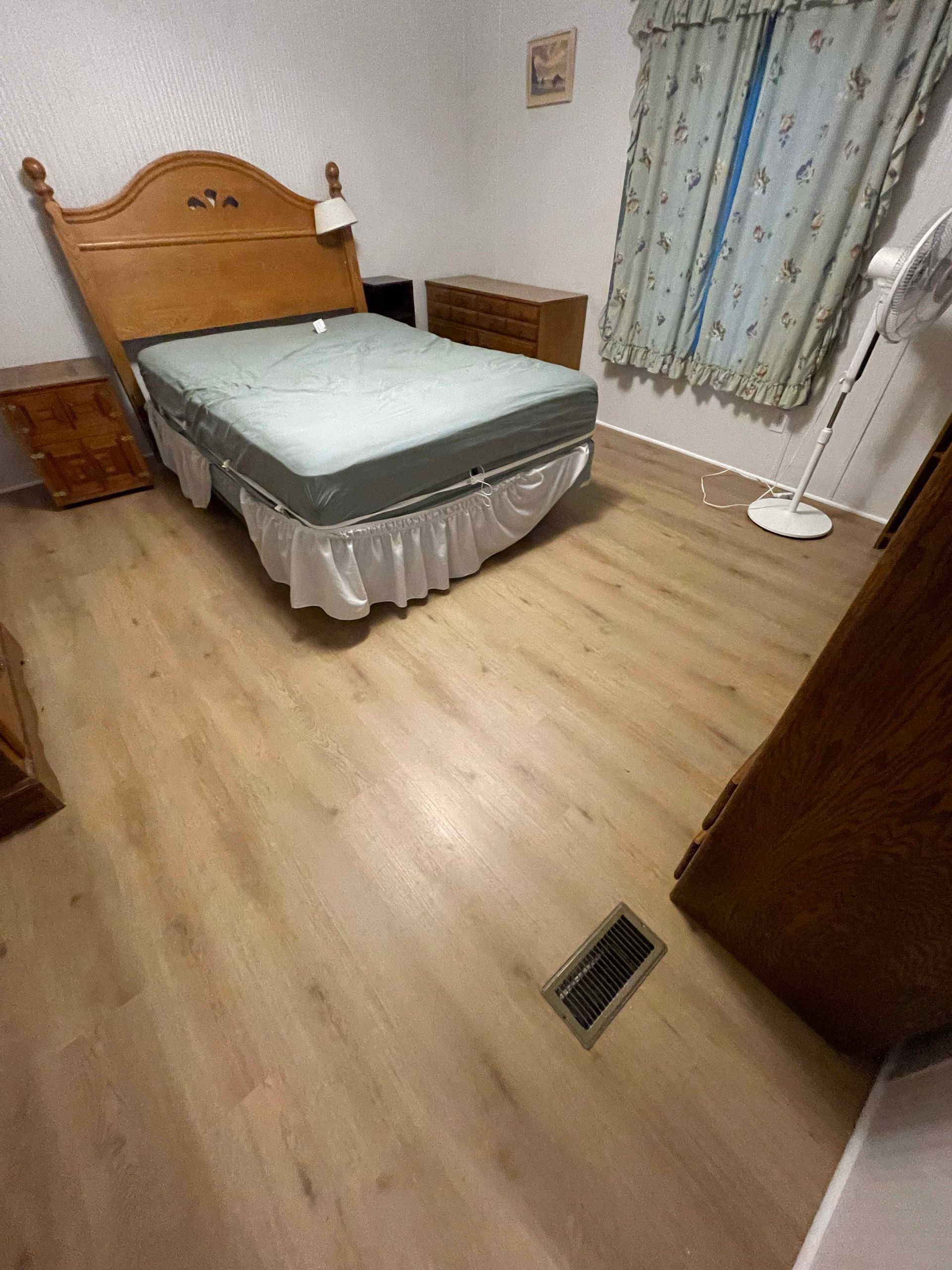 Bedroom with wooden bed, nightstands, dresser, fan, and floral curtains.