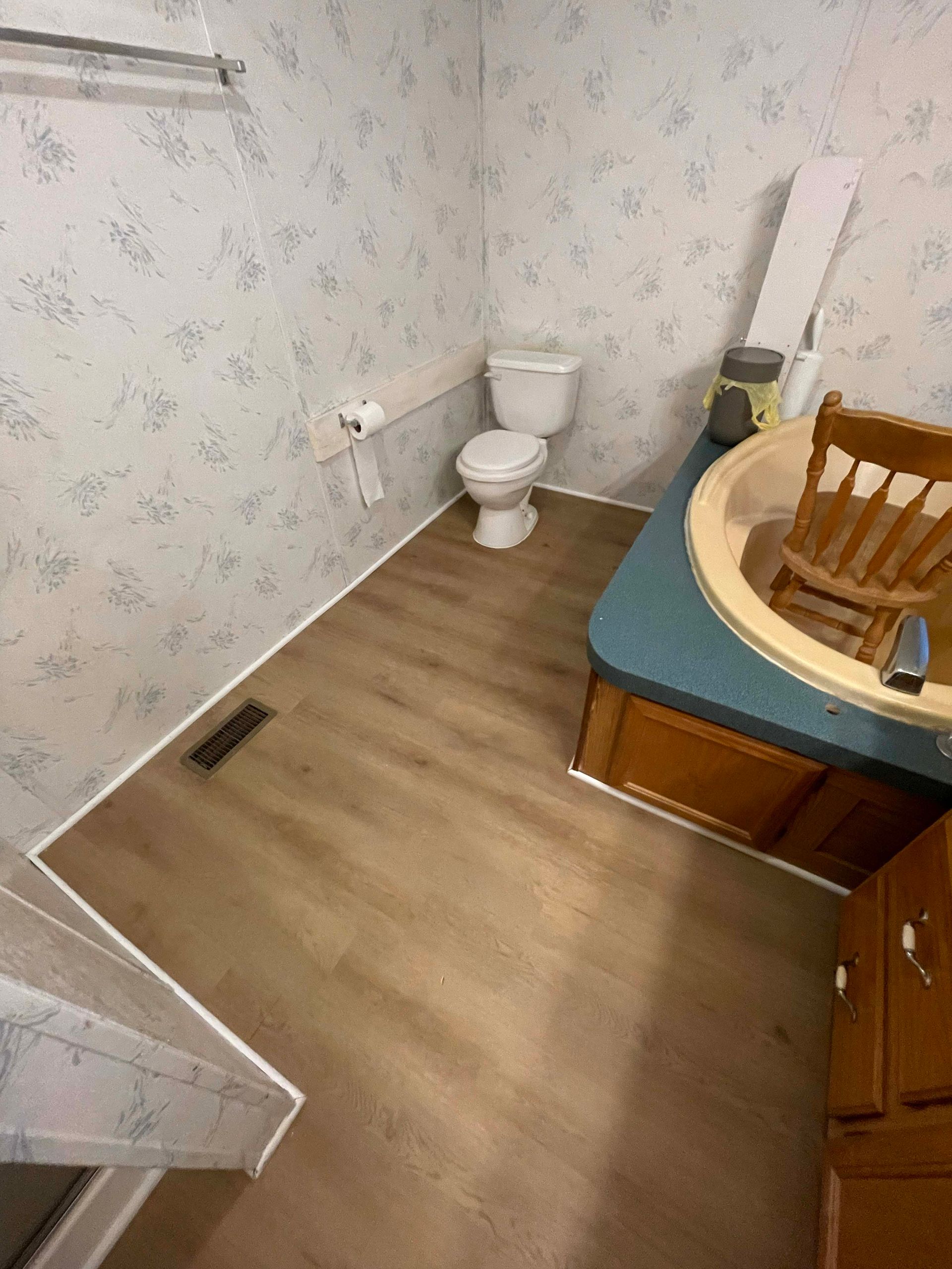Bathroom with toilet, sink, and floral wallpaper. Brown flooring and wooden vanity.