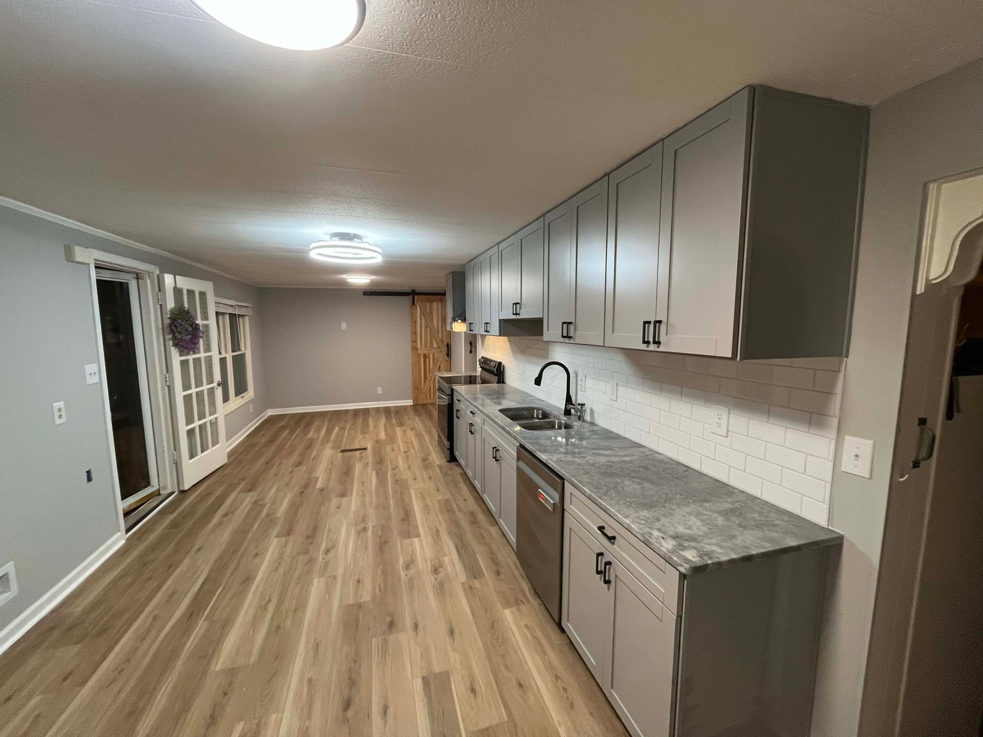 Gray kitchen with long countertops, cabinets, stainless steel appliances, and wood flooring.