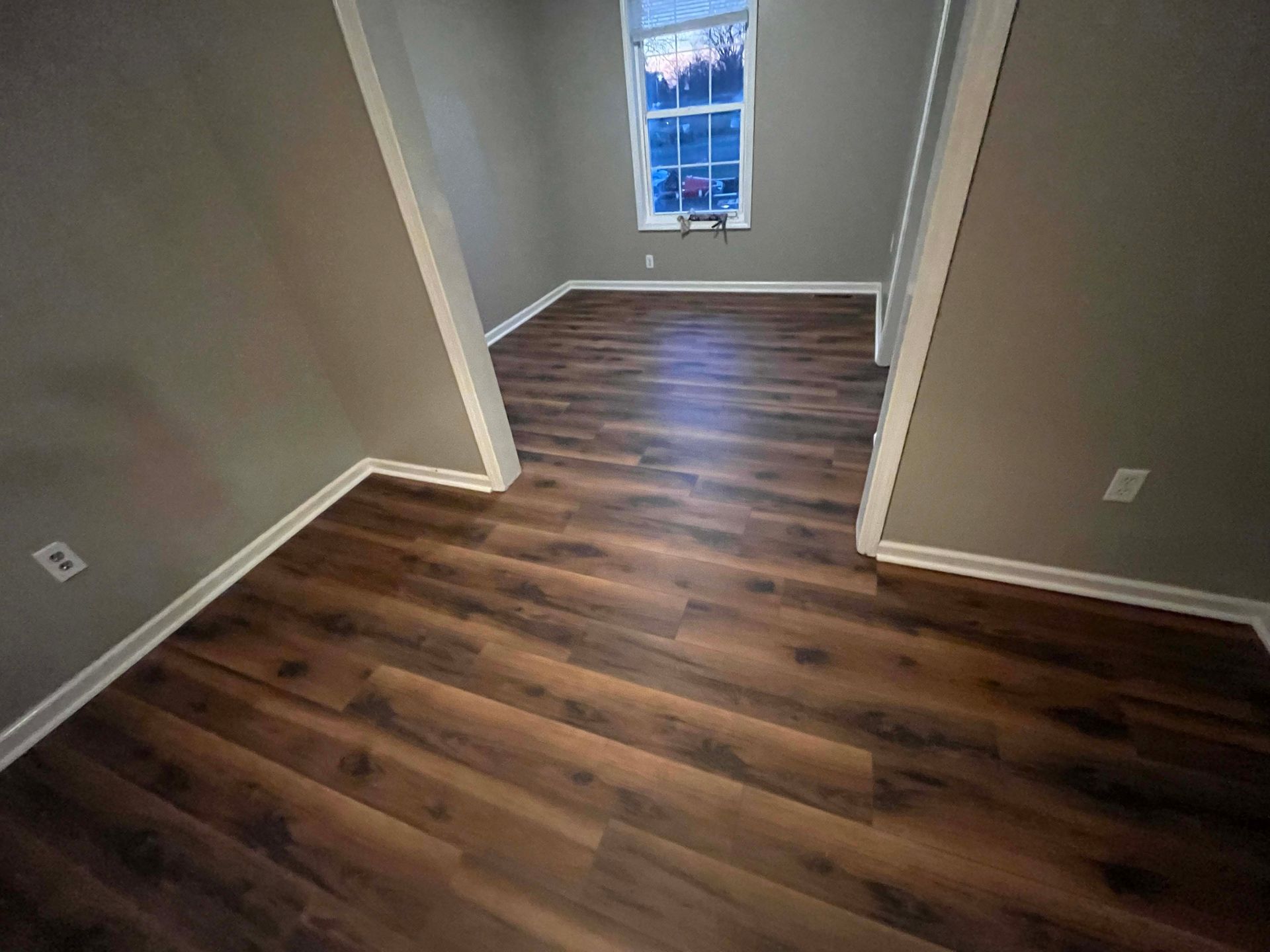 Room with wood-look flooring, gray walls, and white trim. Window lets in light.