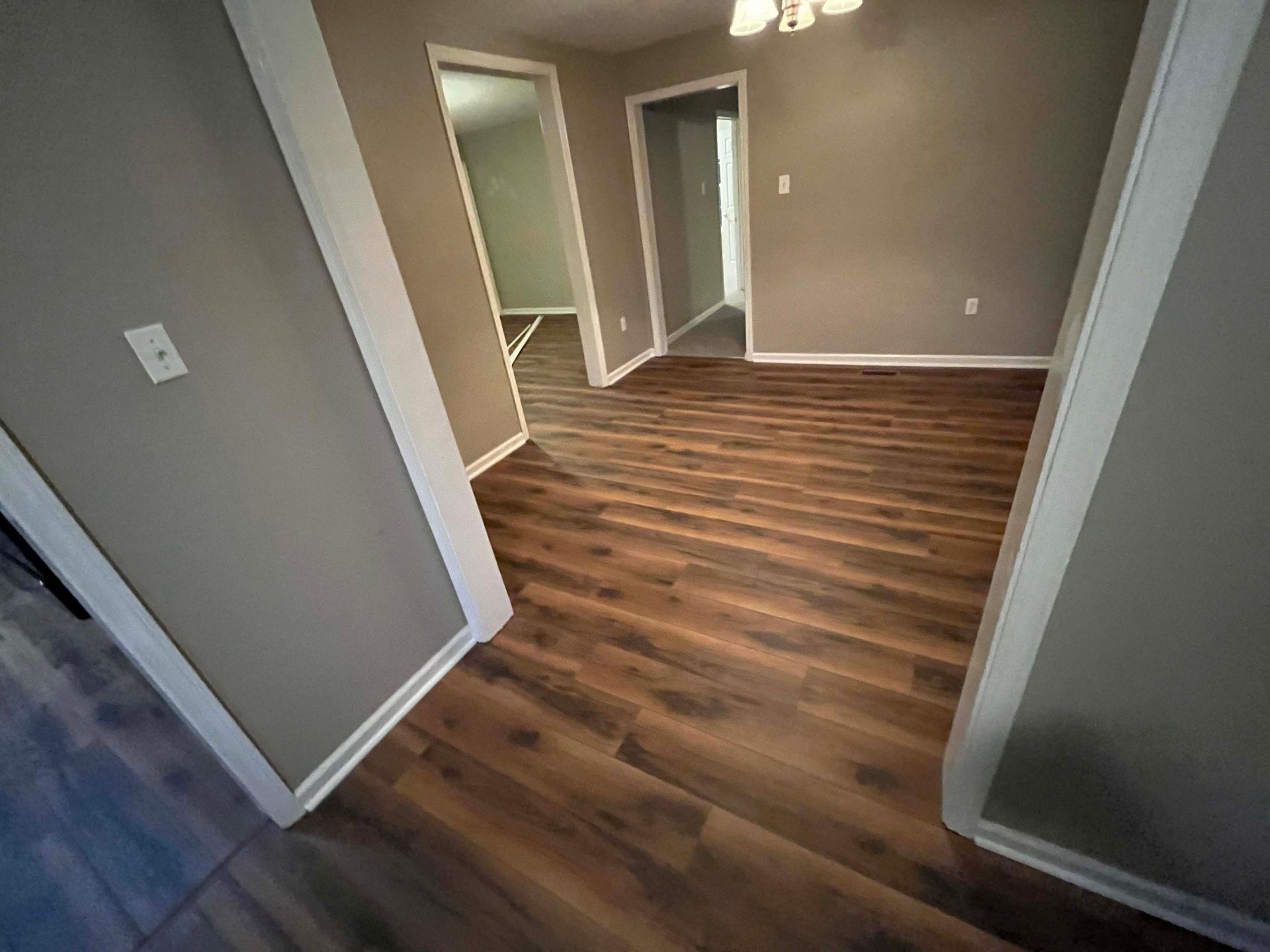 Interior view of a room with wood-look flooring, gray walls, and white trim; doorways lead to other rooms.