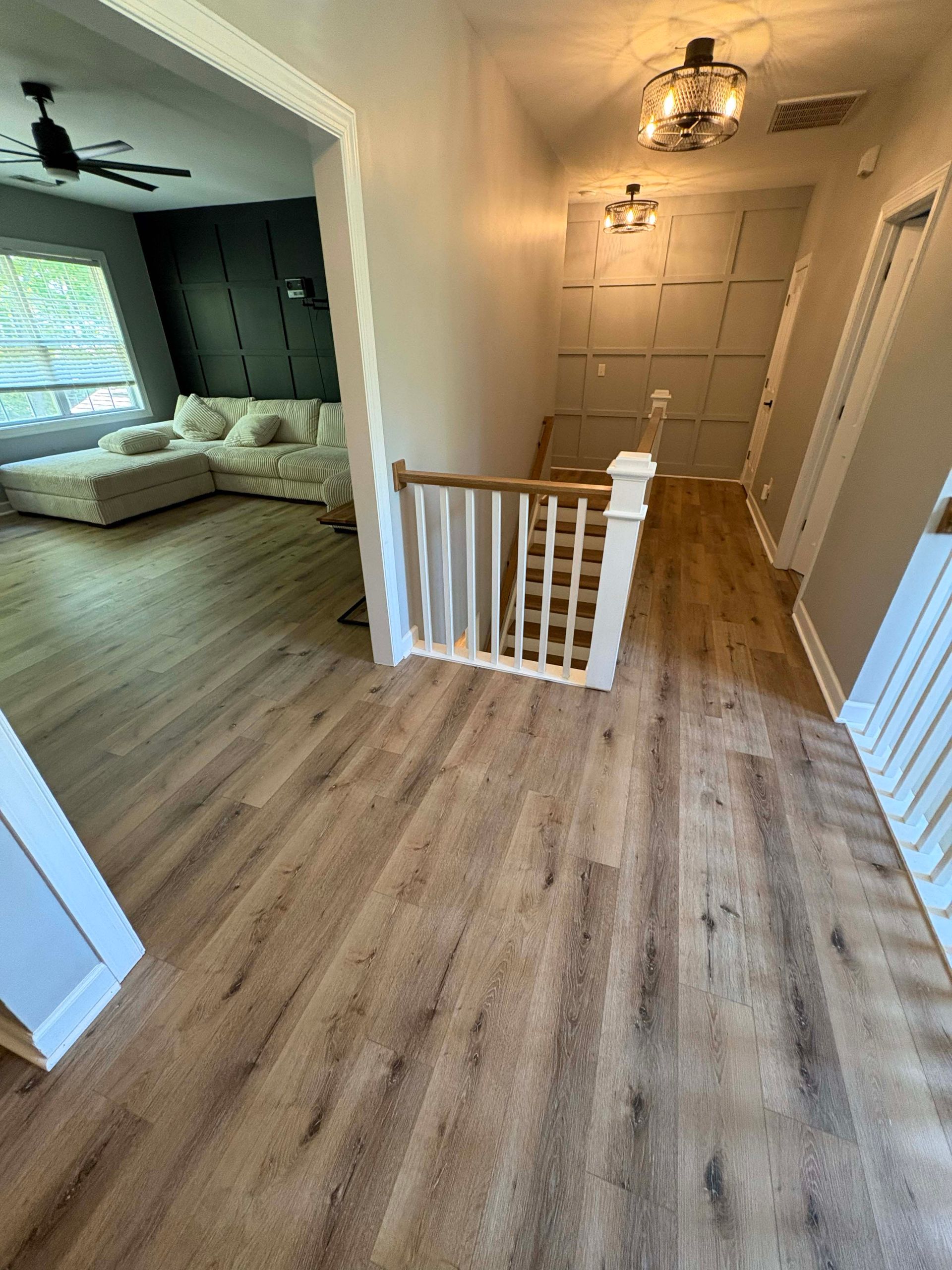 Hallway with wooden floors, stairs, and a living room visible, featuring neutral tones.