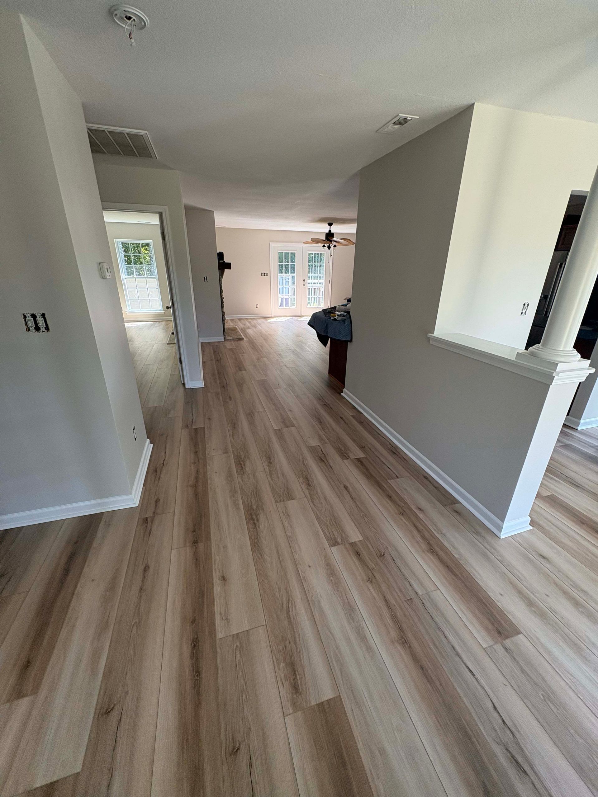 Hallway with light wood-look flooring, light gray walls, and white trim; doors and windows at the end.