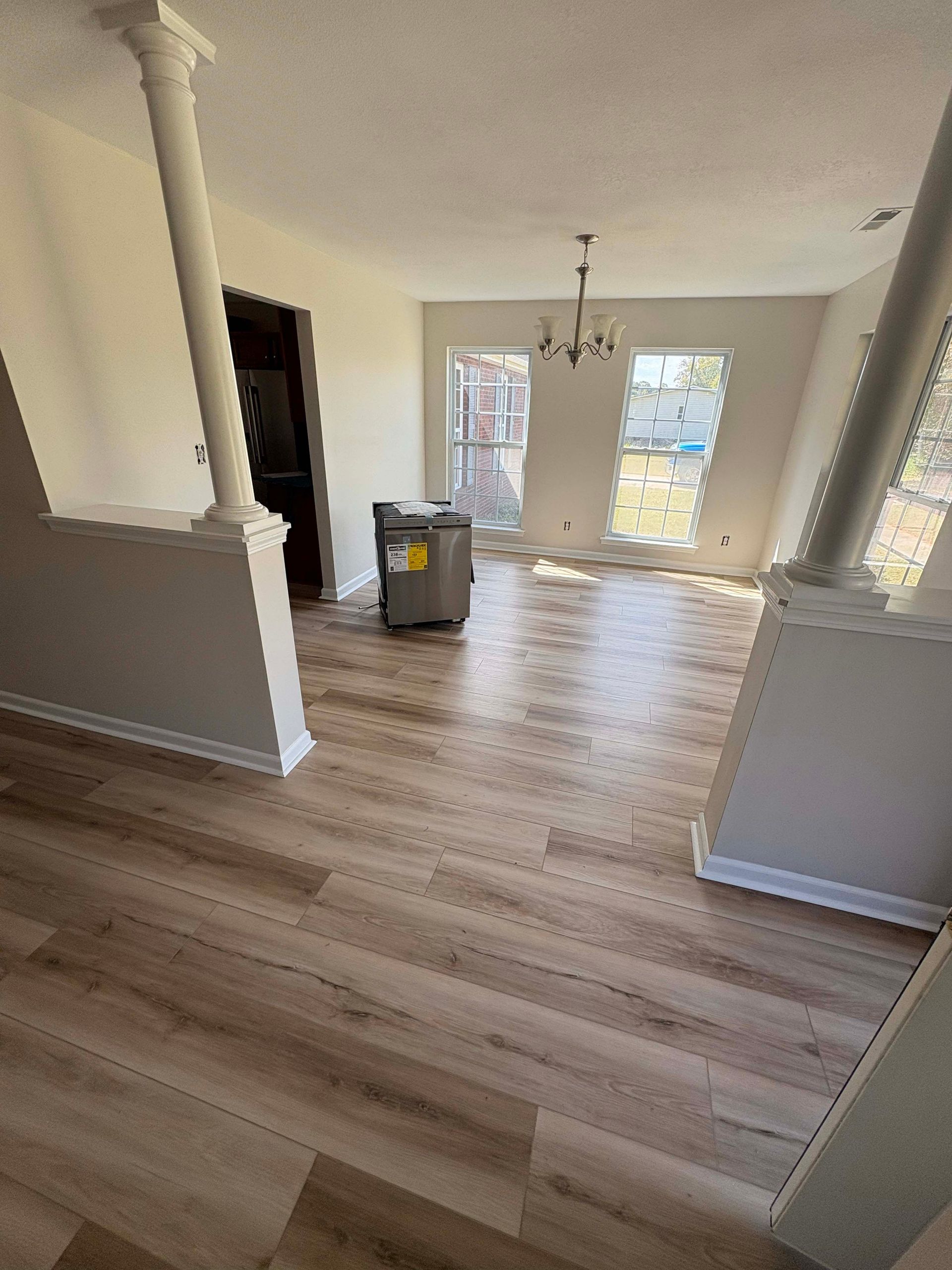 Interior view of a room with wood flooring, pillars, and large windows. There's a washing machine visible.