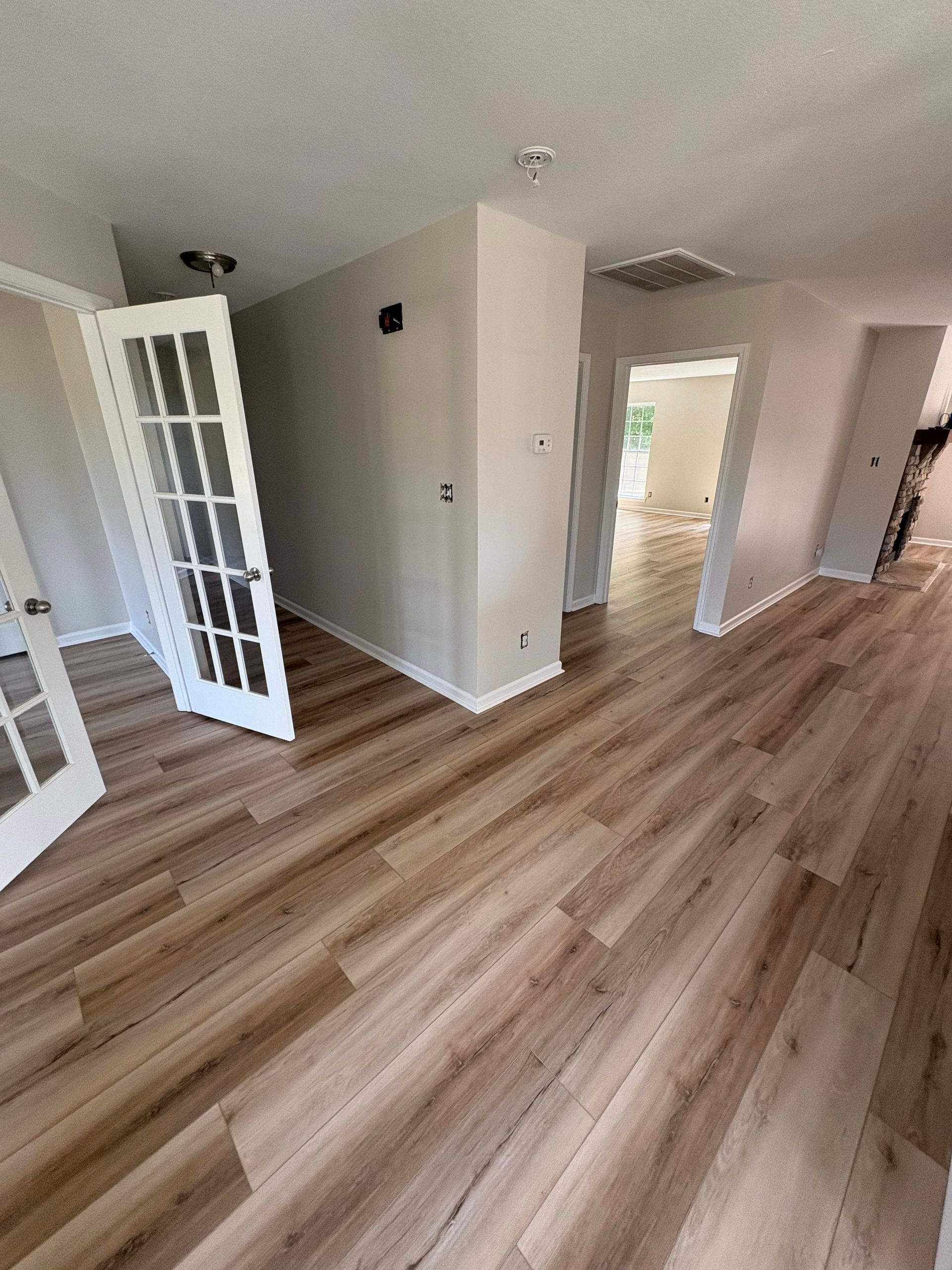 Interior view of a room with wood-look flooring, light gray walls, and white French doors.
