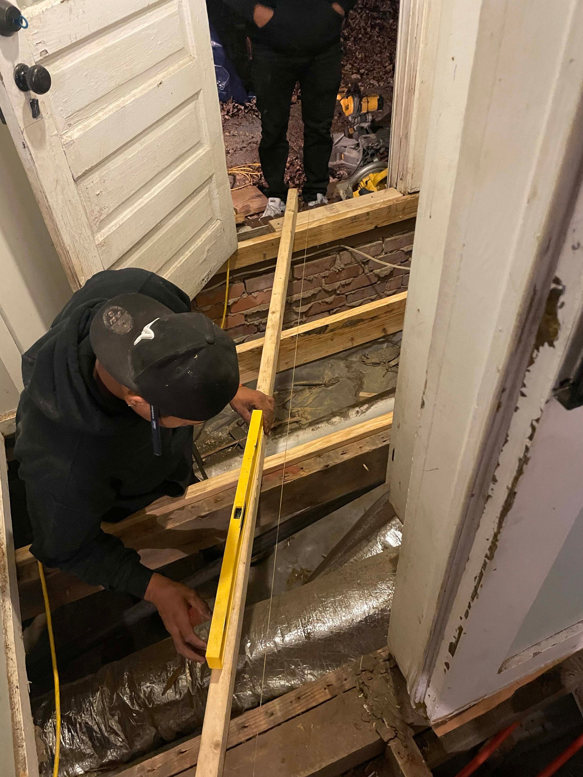 Person using level on wooden beams during floor renovation.