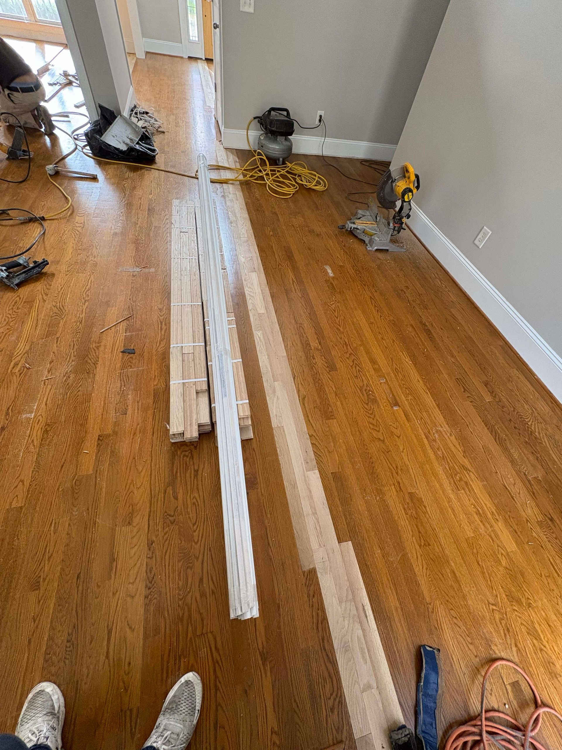 Hardwood floor installation in progress, with tools and new wood planks on existing floor.