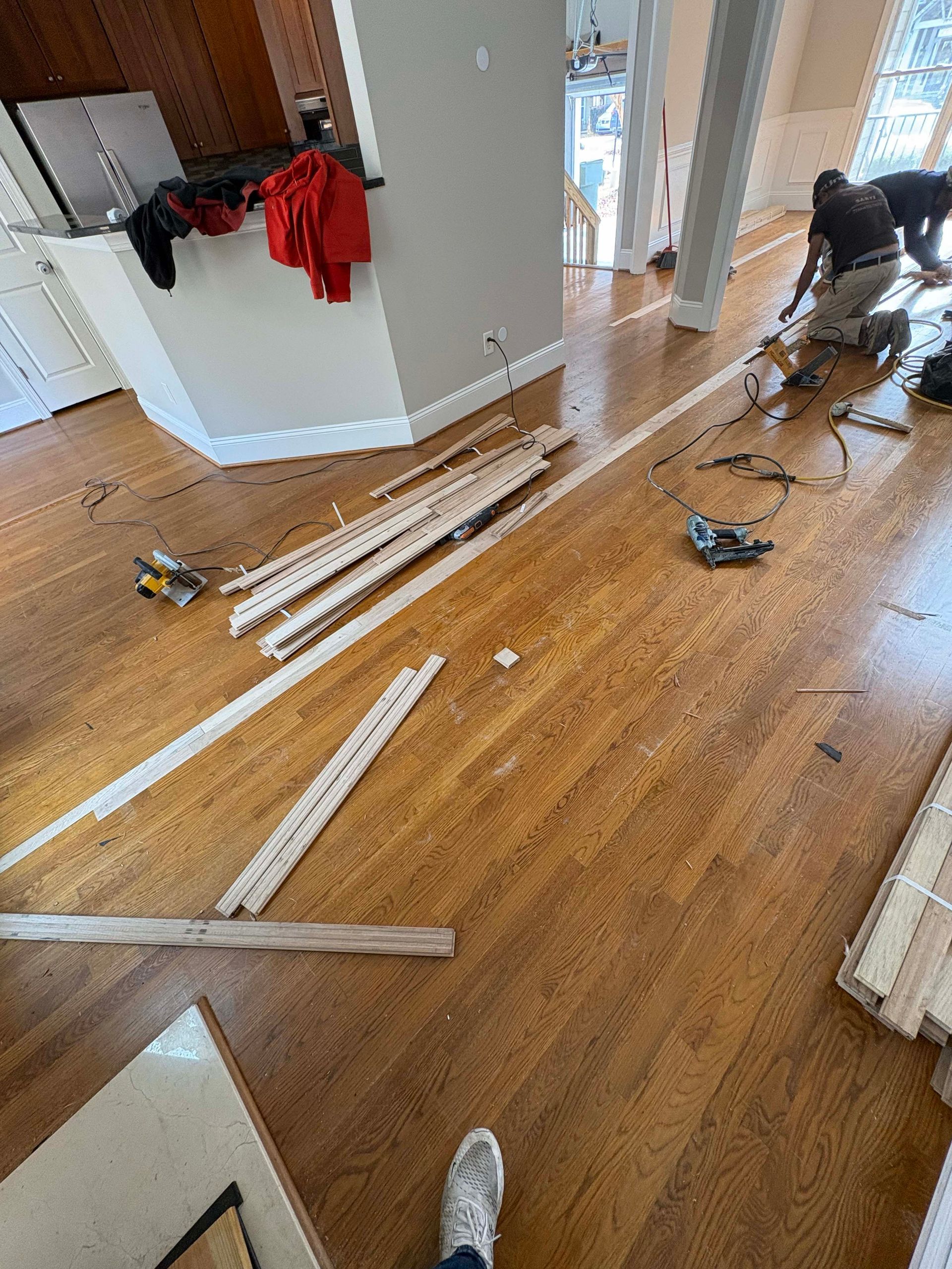 Hardwood floor installation in progress, with tools and workers in a room with a white wall and trim.