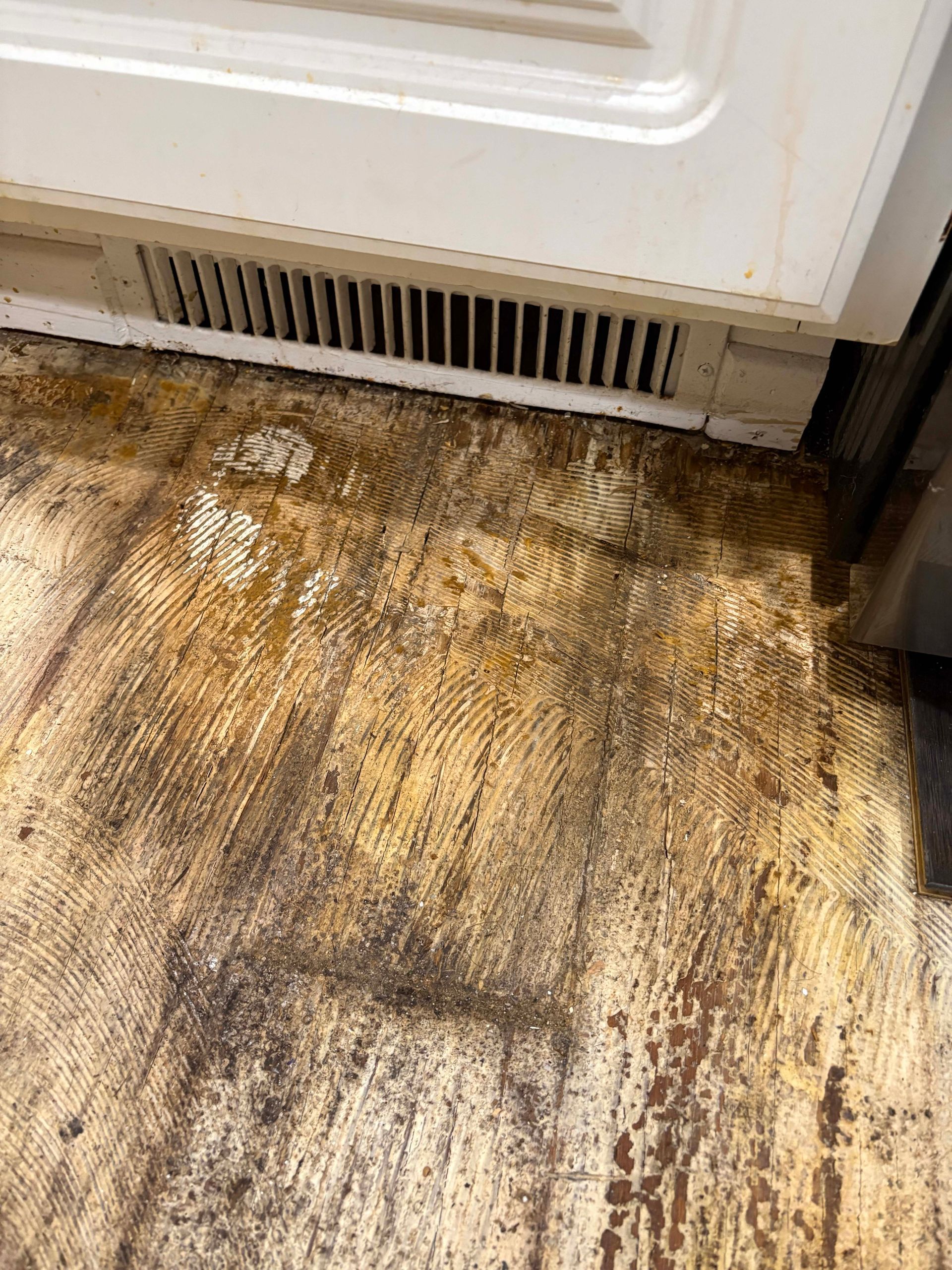 Wooden floor damaged by water, below a white cabinet with a vent.