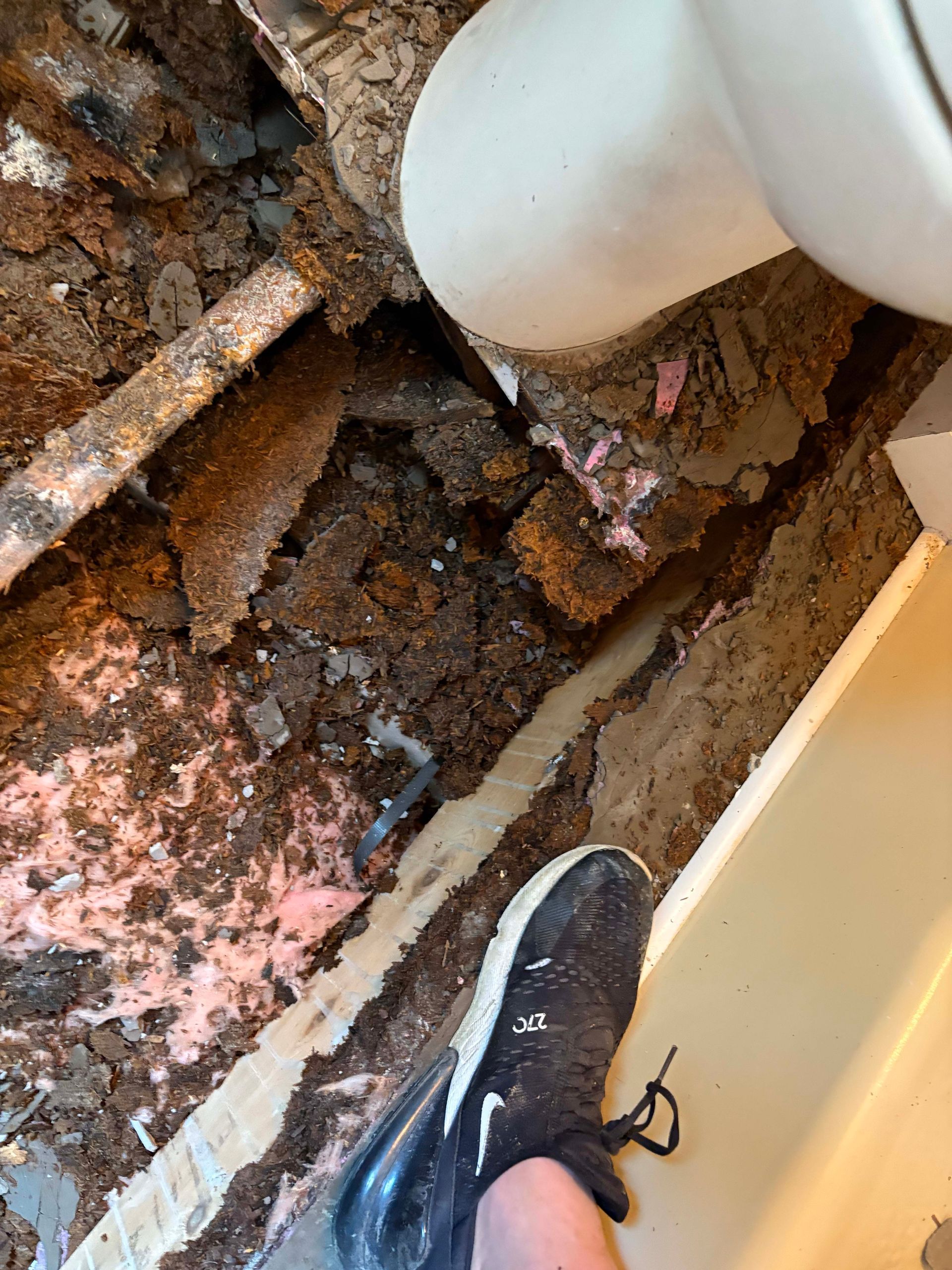 Foot next to damaged bathroom structure; exposed pipes, insulation, and debris.