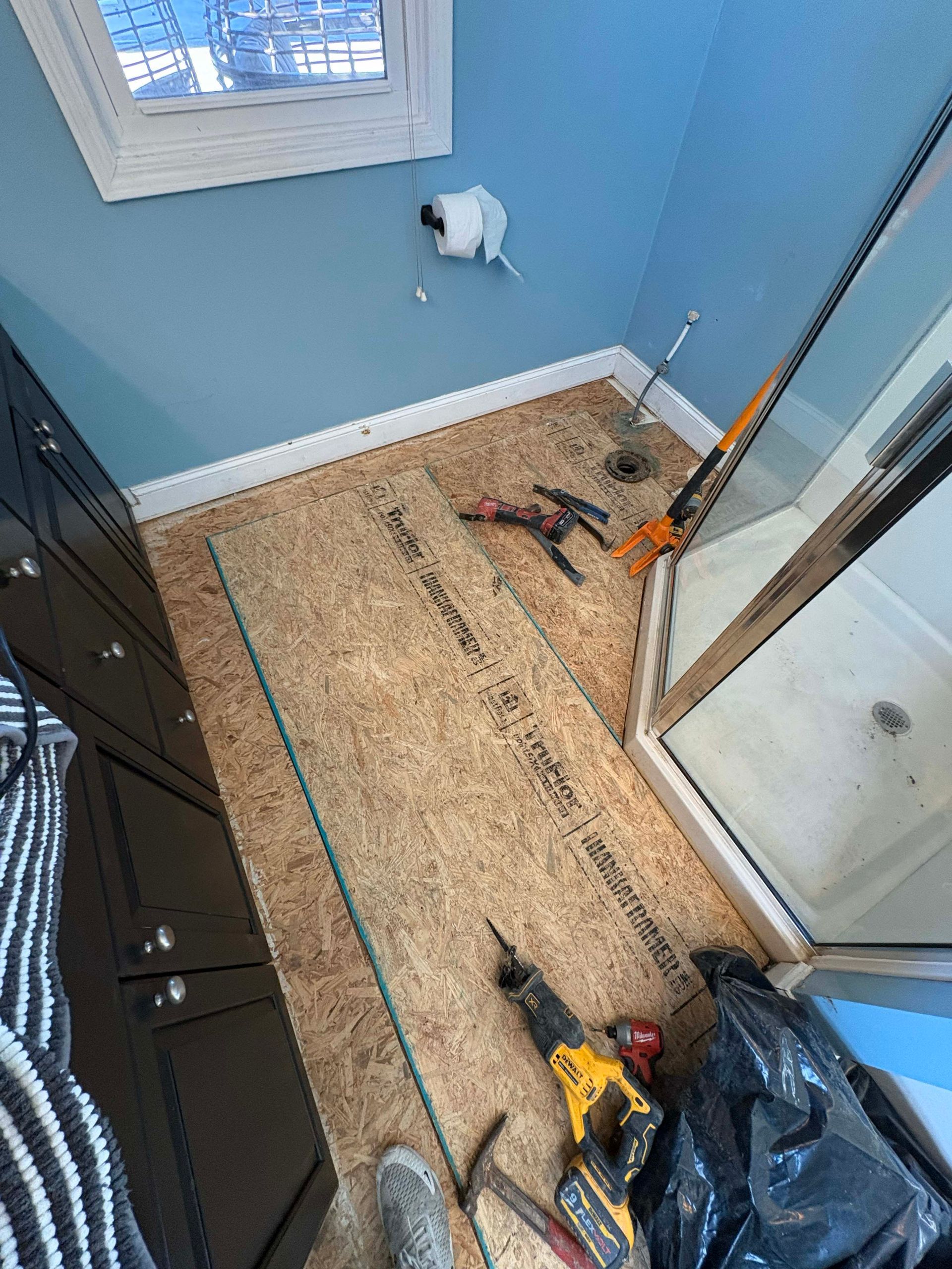 Bathroom renovation in progress. Cork flooring installed near shower and cabinets. Tools and debris present.