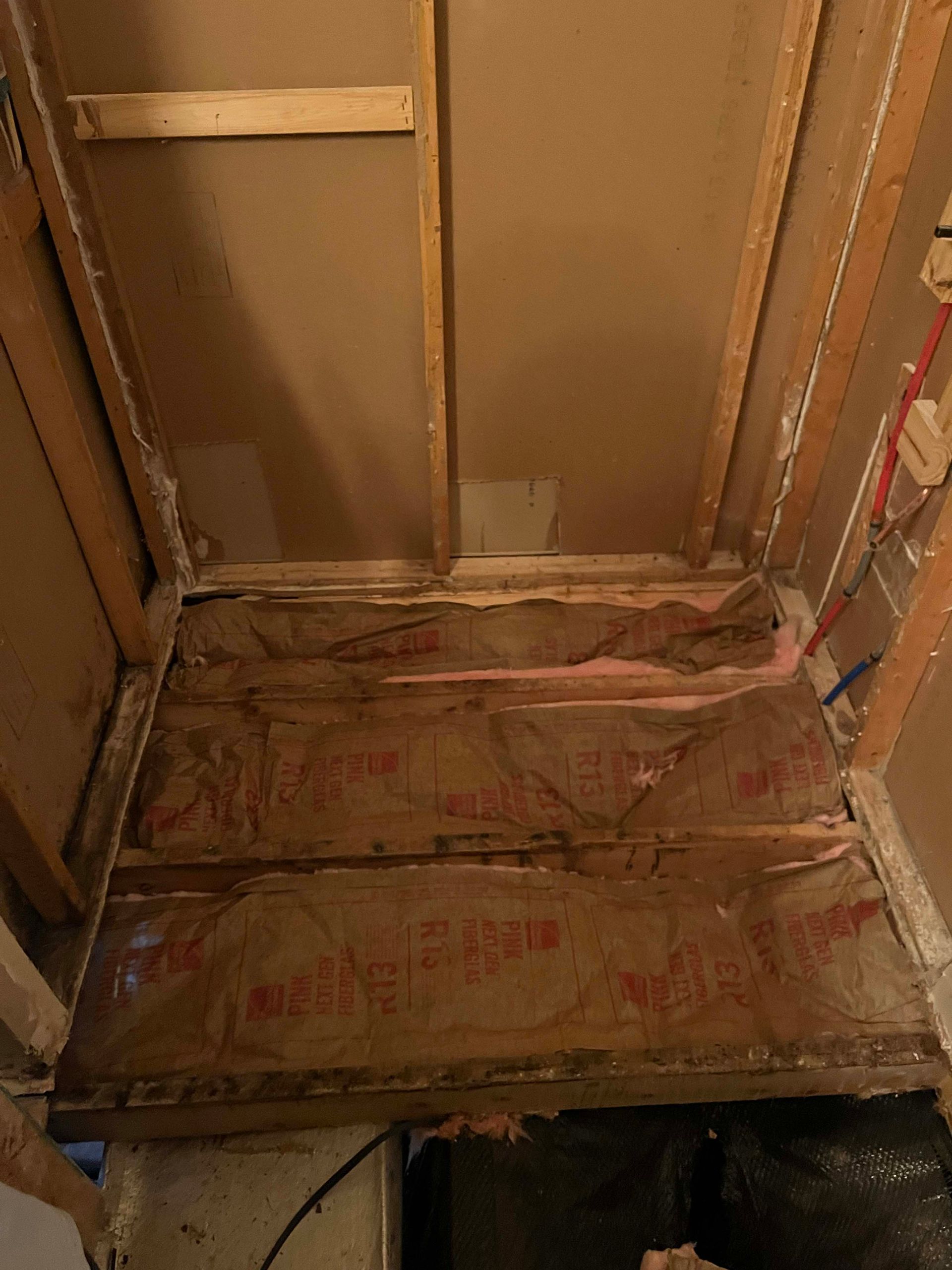 Open bathroom shower frame with exposed wooden supports, insulation, and unfinished walls.