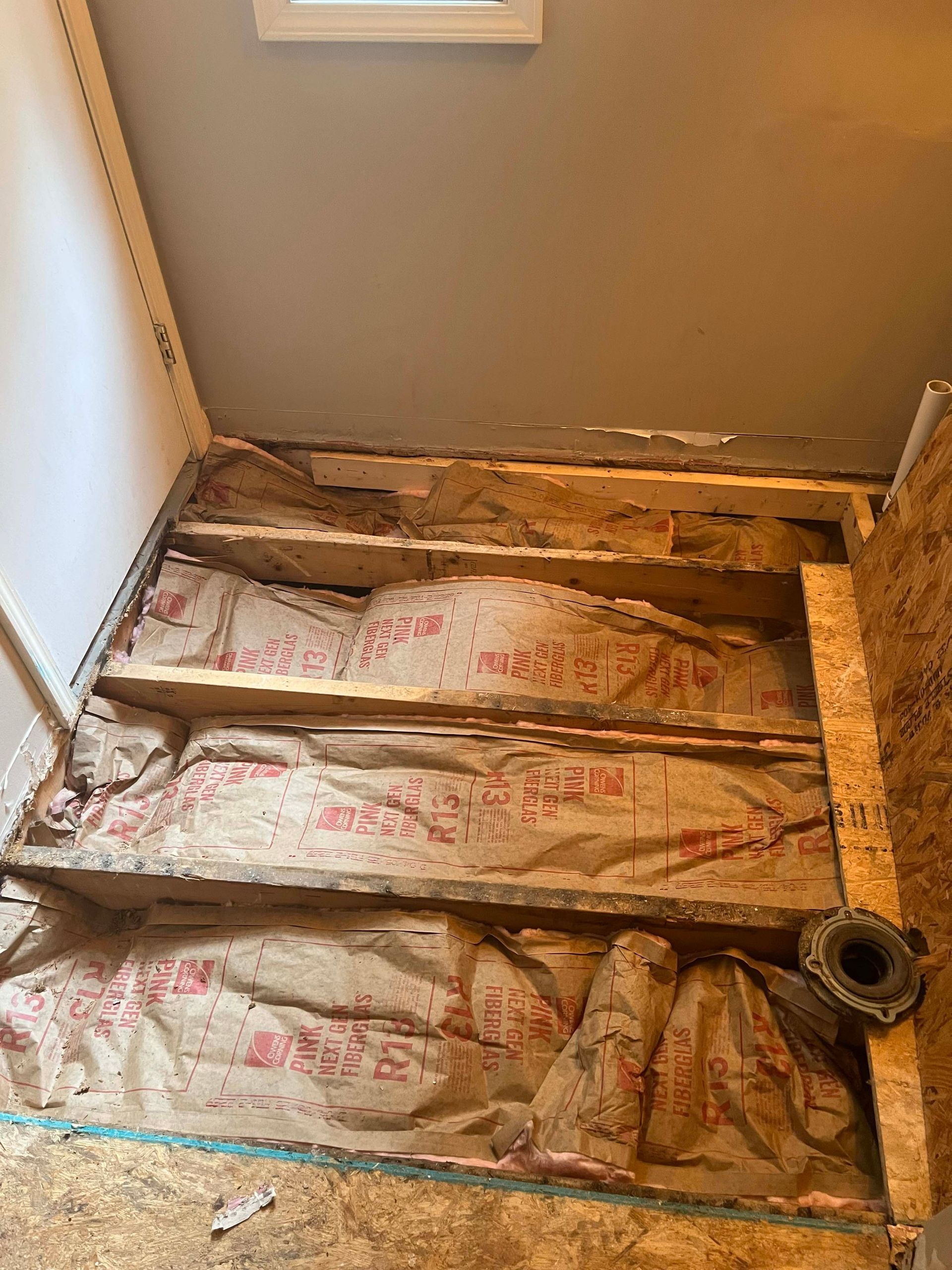 Bathroom floor under construction, exposed joists, insulation, unfinished walls.