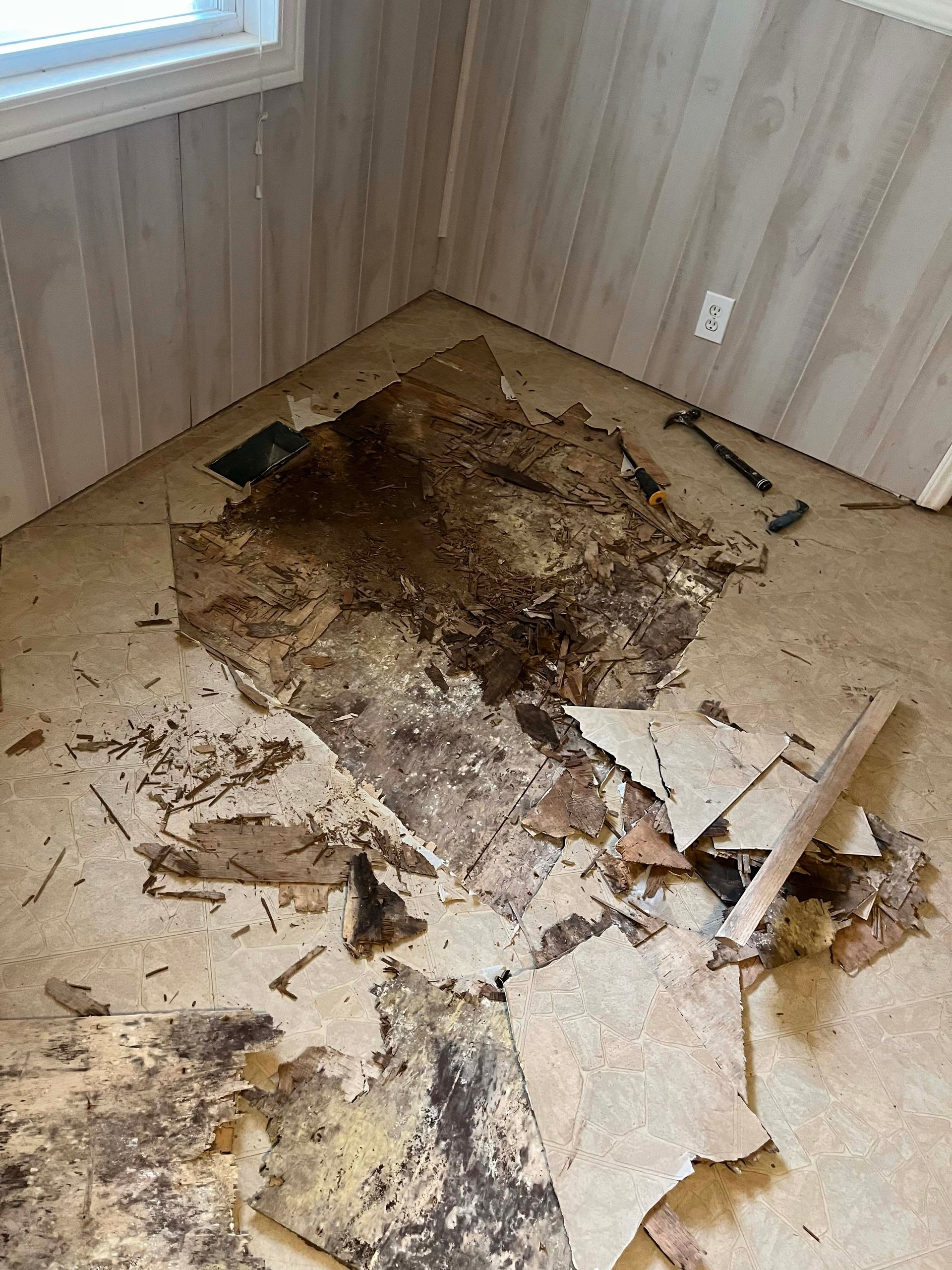 Debris from torn up flooring in a corner of a room, hammer and debris visible.