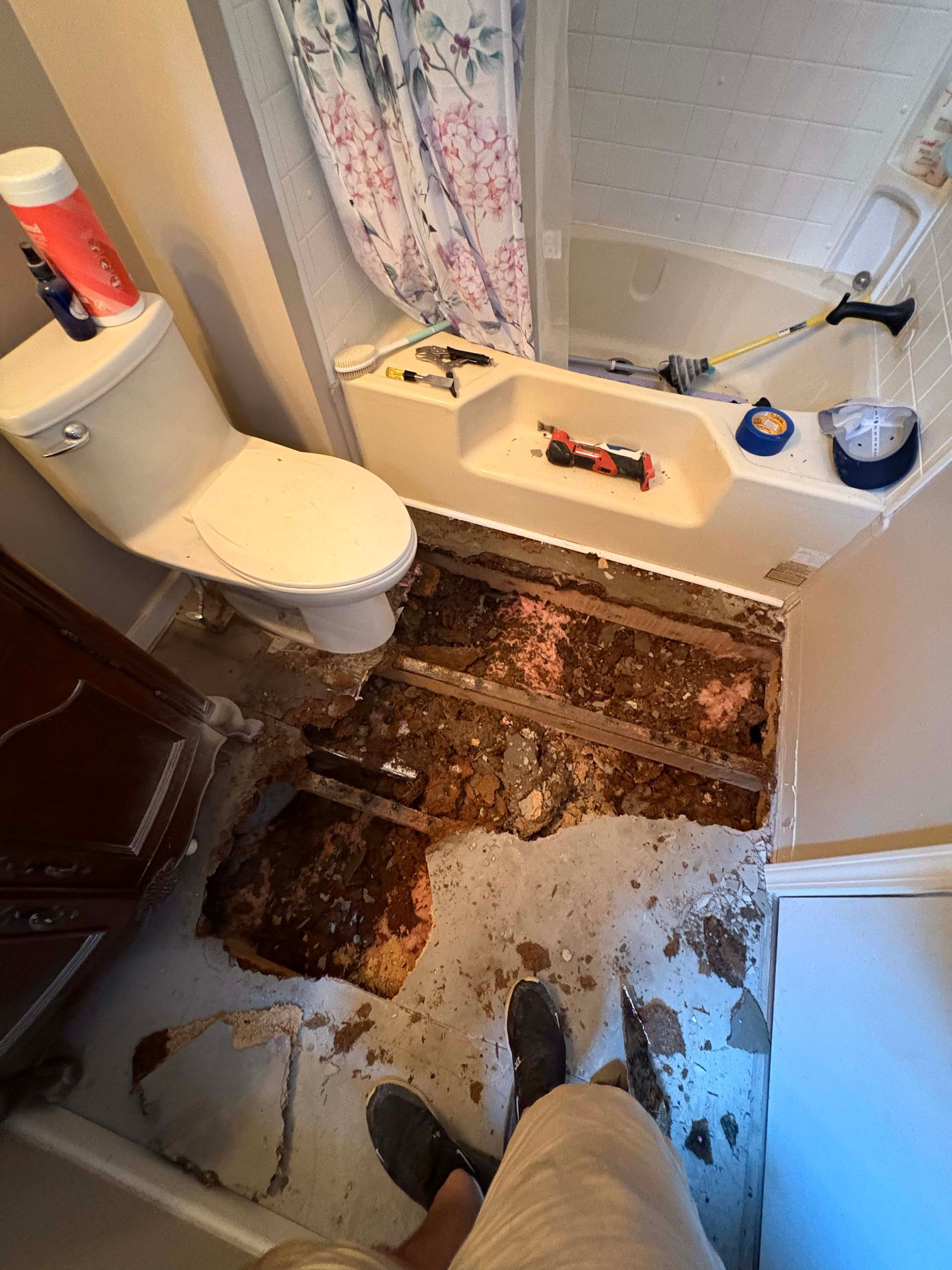 Bathroom with severely damaged floor and exposed joists; toilet, bathtub, and tools visible.
