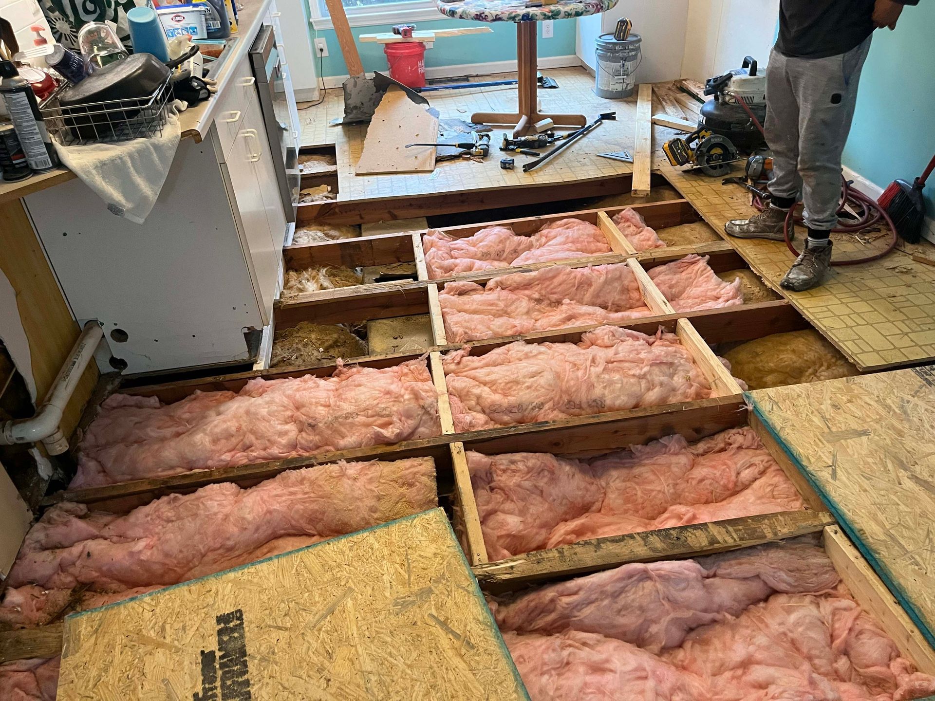 Flooring being renovated; pink insulation between floor joists; person standing.