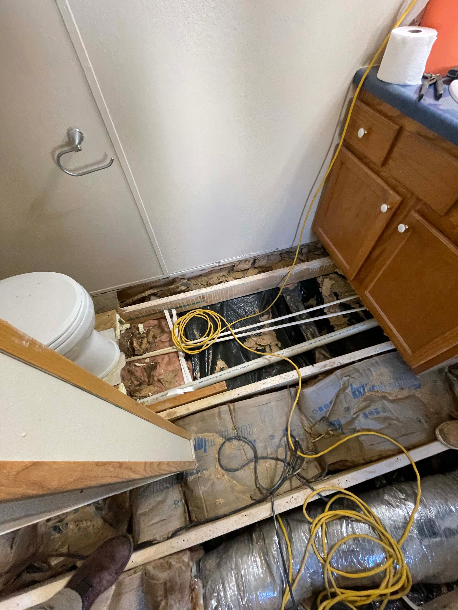 Damaged RV floor exposing insulation and wiring. Toilet, cabinets, and rolled-up insulation are visible.