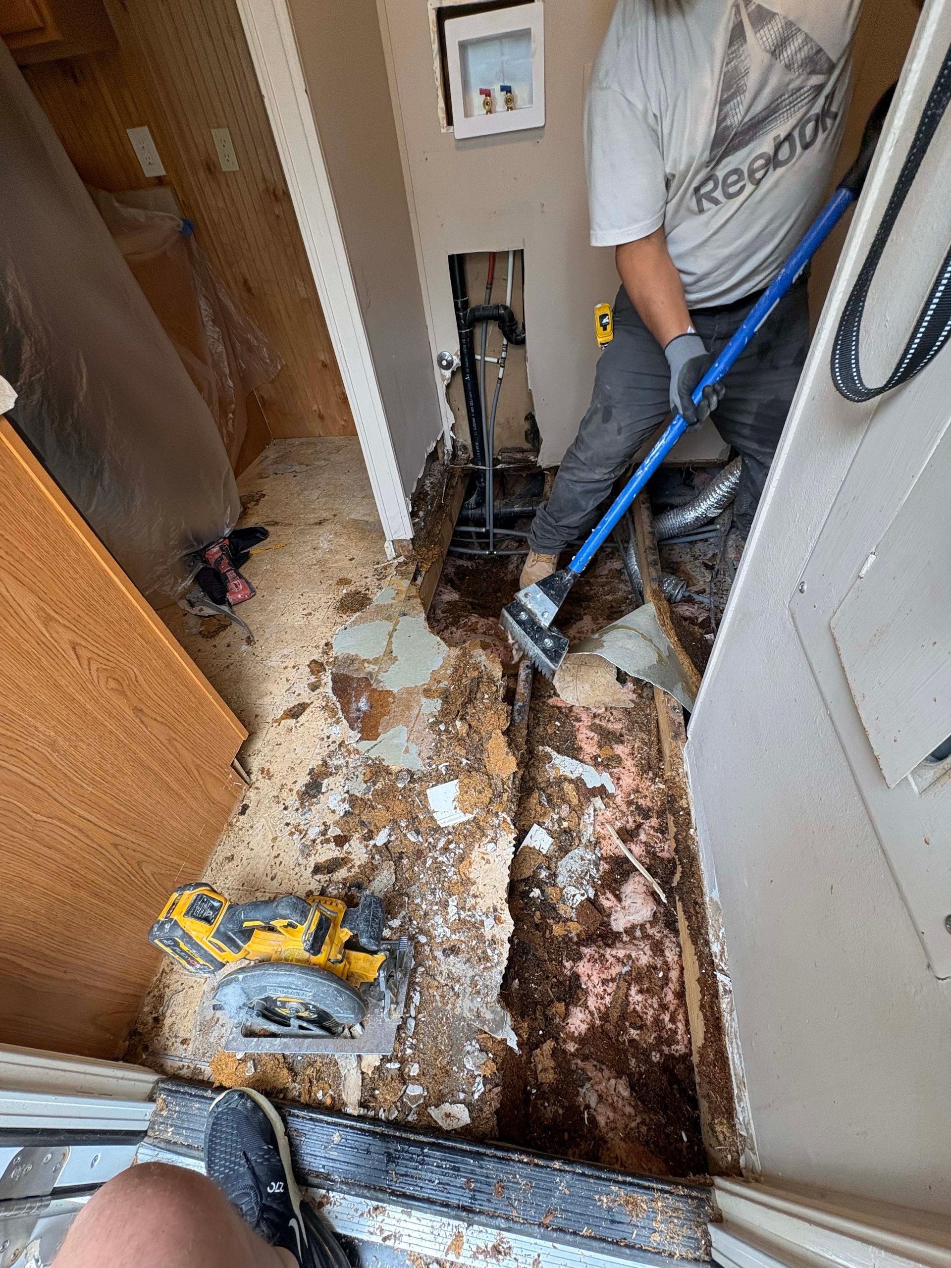 Man removing flooring with a tool, exposed subfloor, construction site.