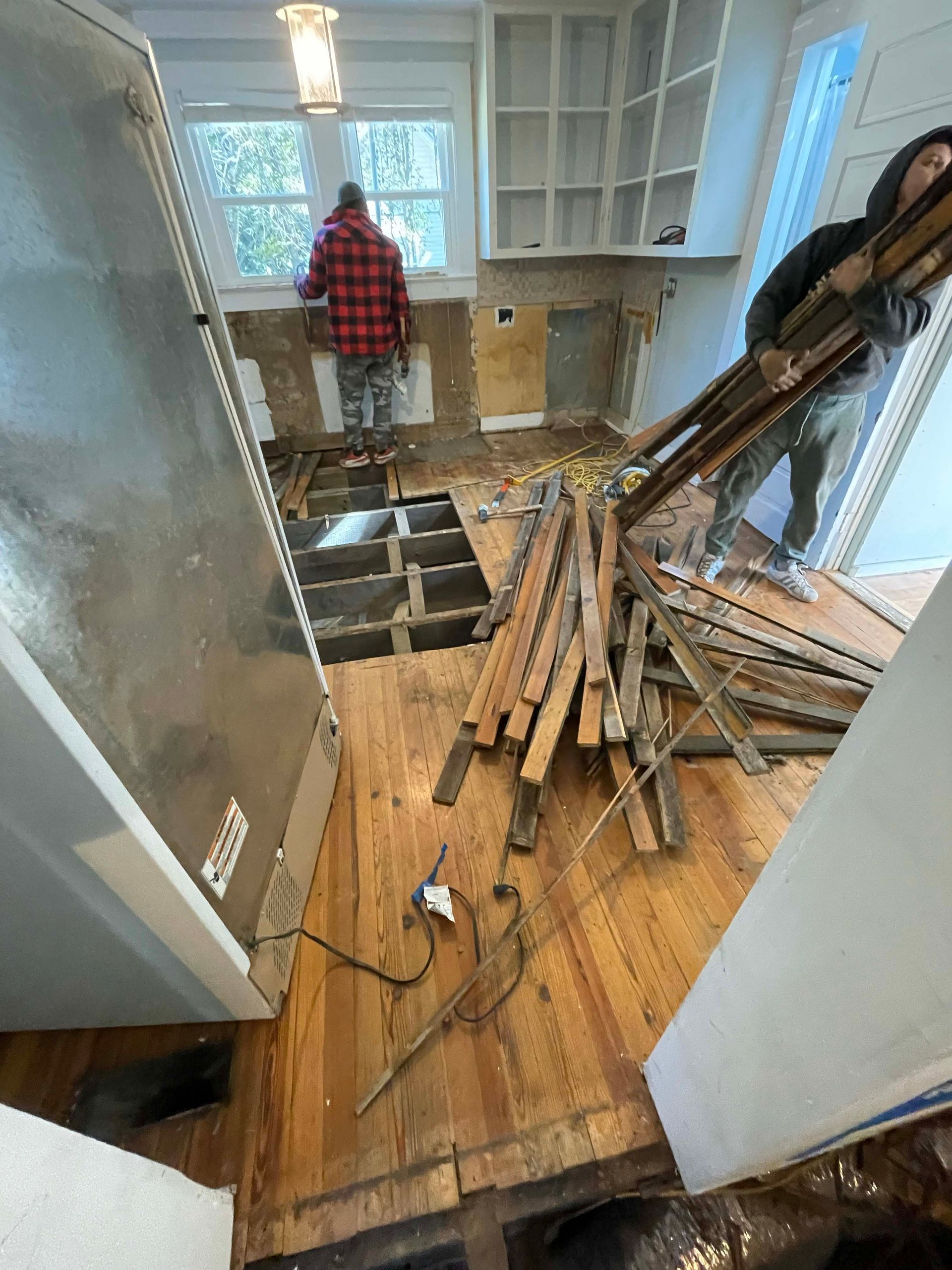 Kitchen remodel in progress: debris on wooden floor, workers, partially demolished cabinets.