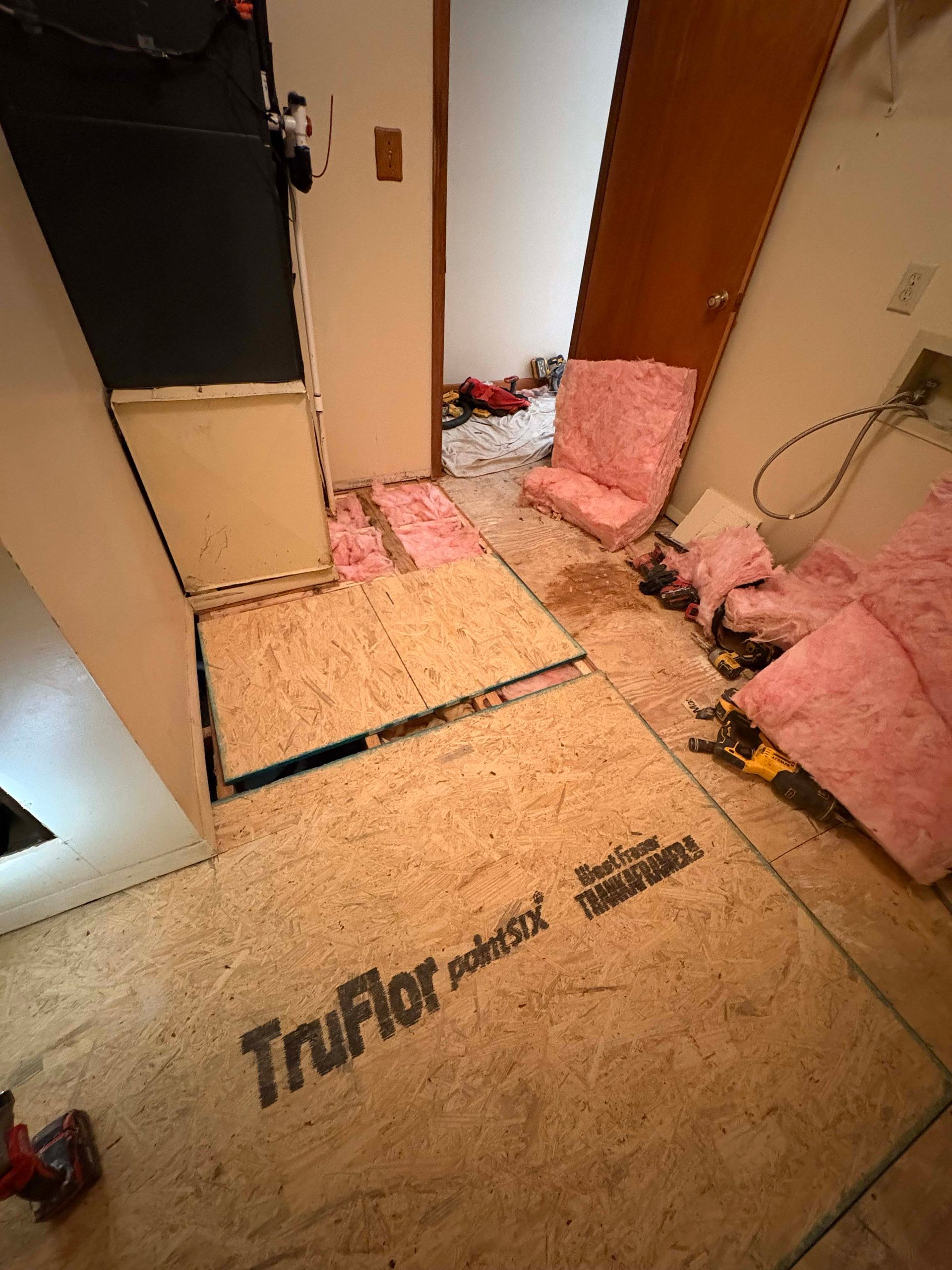 Room under renovation; exposed subfloor, insulation, and partially dismantled walls.