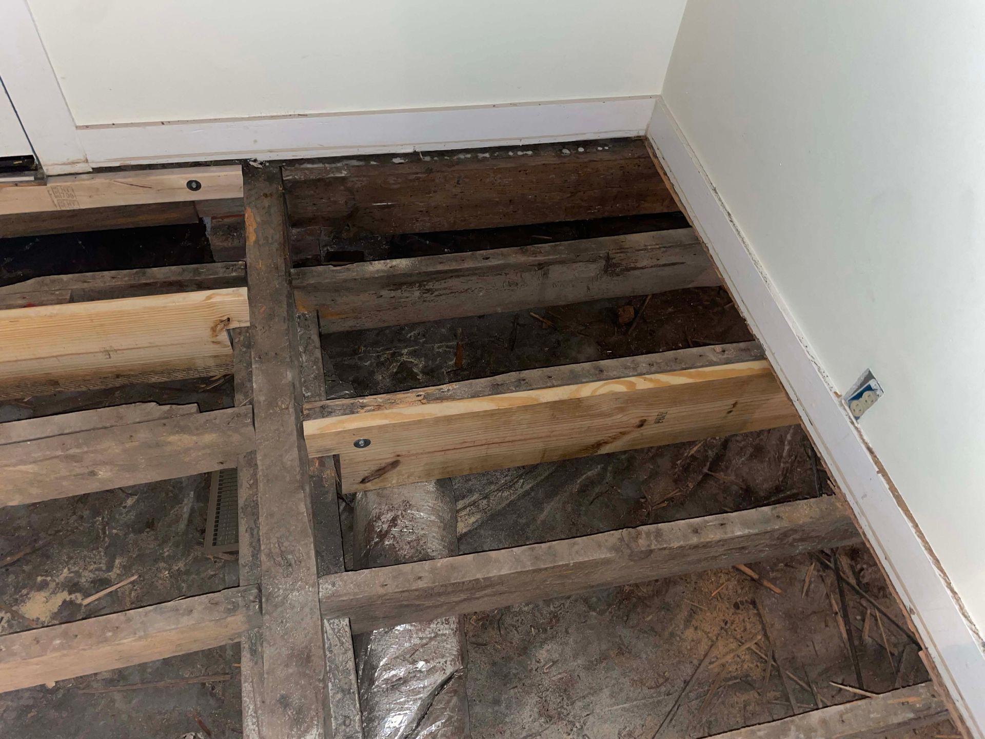 Exposed wooden floor joists in a room with white walls. Plastic sheeting covers the space below.