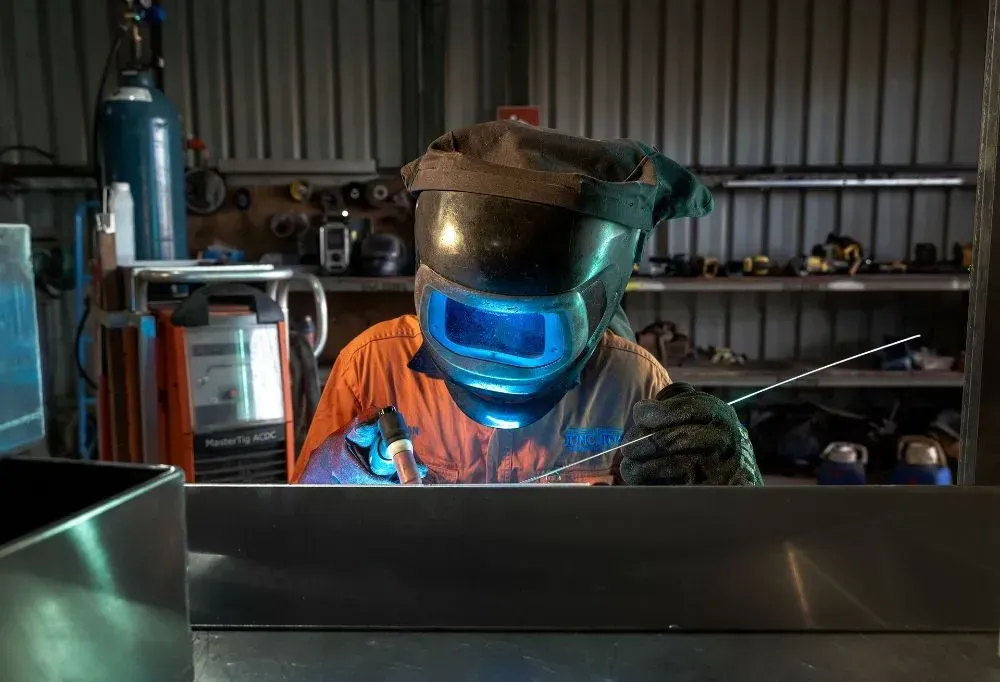 Welder in a Workshop, Wearing a Helmet and Gloves, Welding Metal — Junction Engineering Group in Evans Landing, QLD