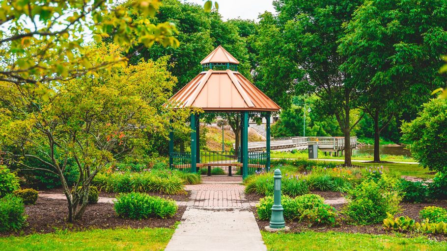 Gazebo in a lush green park with a stone path and trees around it