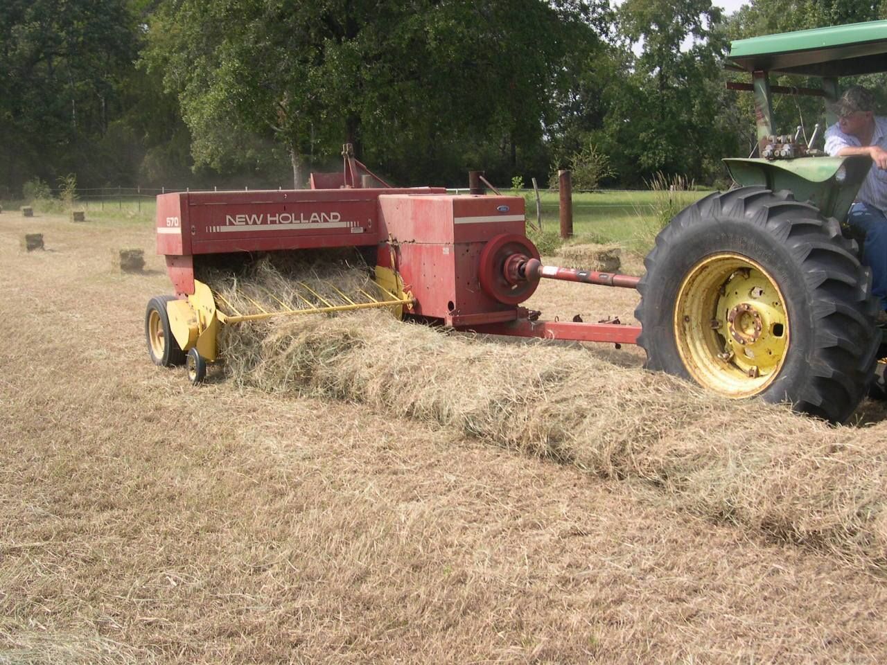 Red hay baler attached to a tractor compressing hay in a field