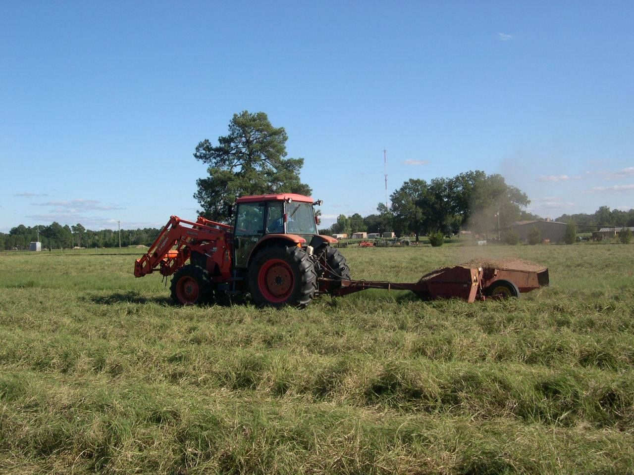 Red tractor mowing grass in a field under a clear blue sky.