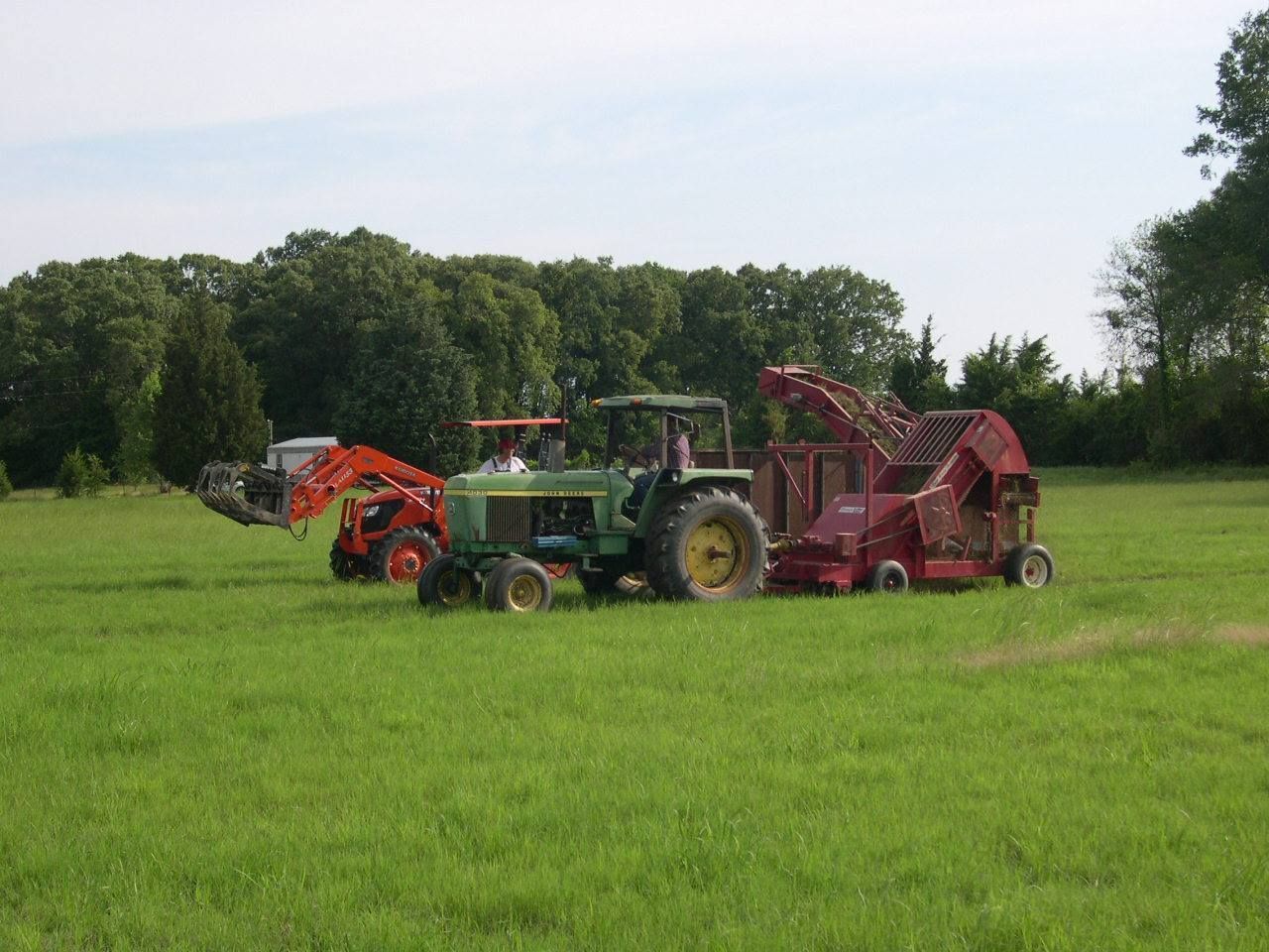 Tractors and farm machinery in a green field with trees in the background